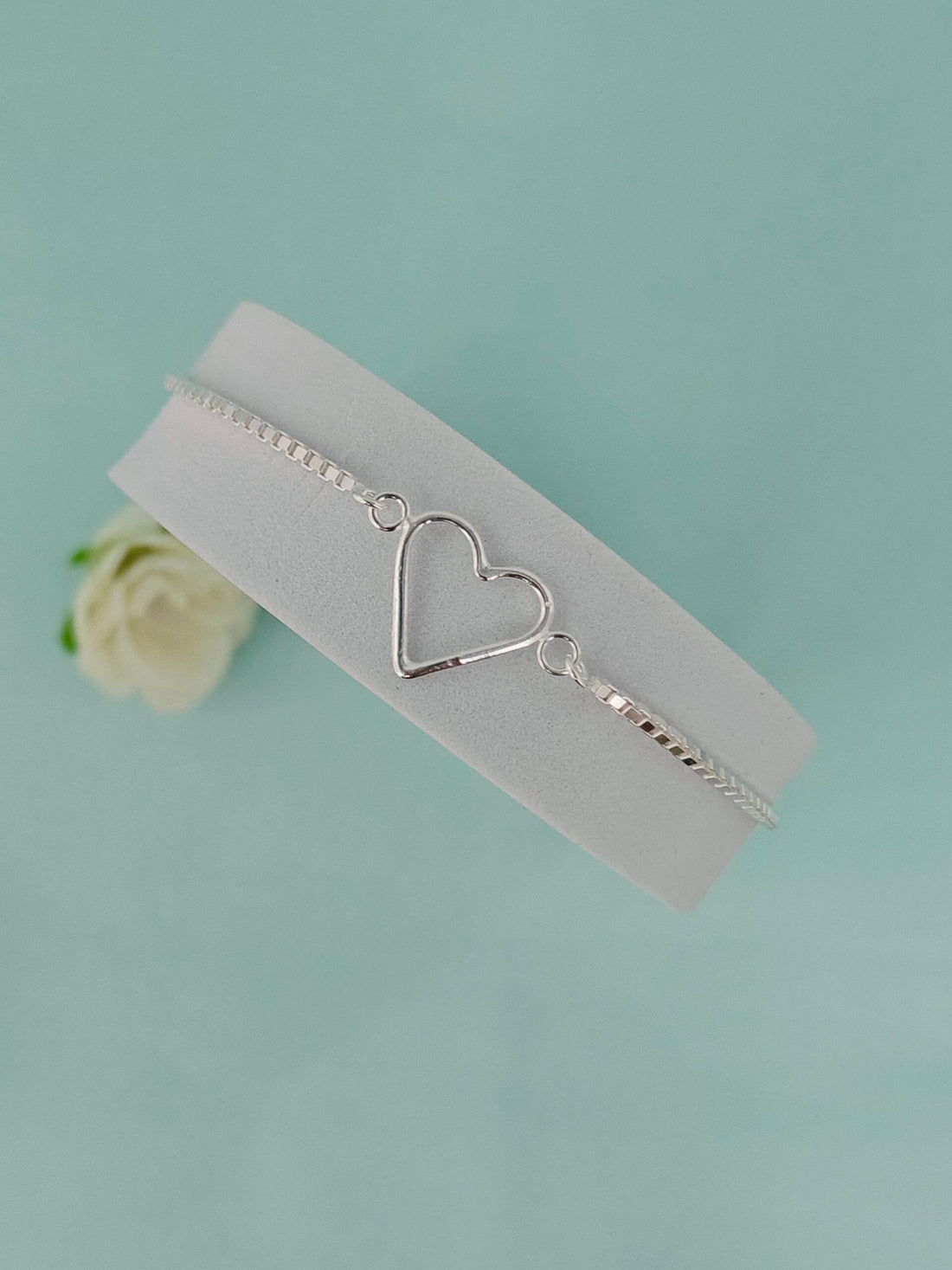 Silver bracelet with a heart charm on a light blue background