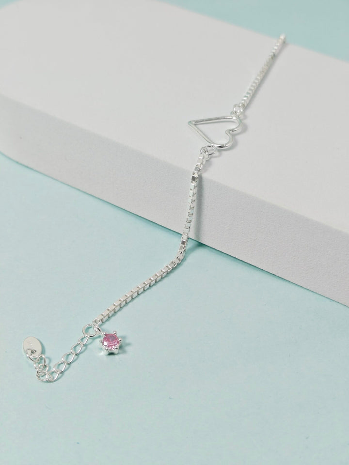 Silver bracelet with a pink heart charm on a light blue and gray background