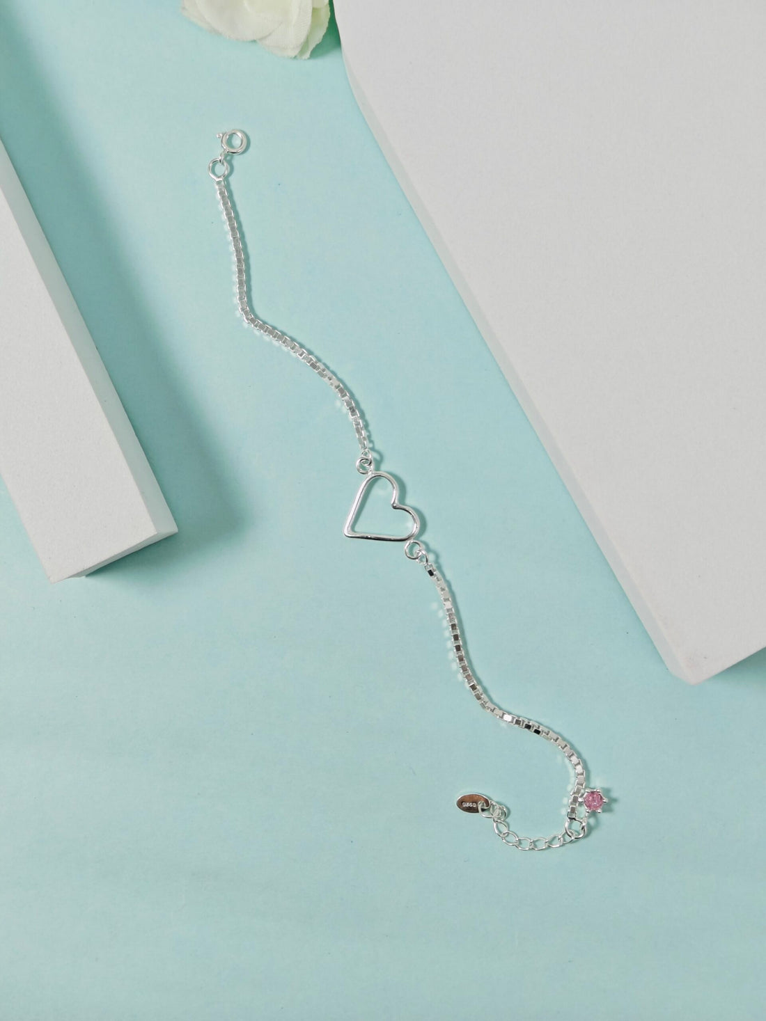 Silver bracelet with a heart charm on a light blue surface