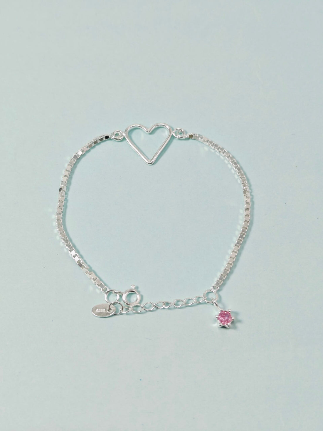 Silver bracelet with a heart-shaped clasp and pink charm on a light gray background
