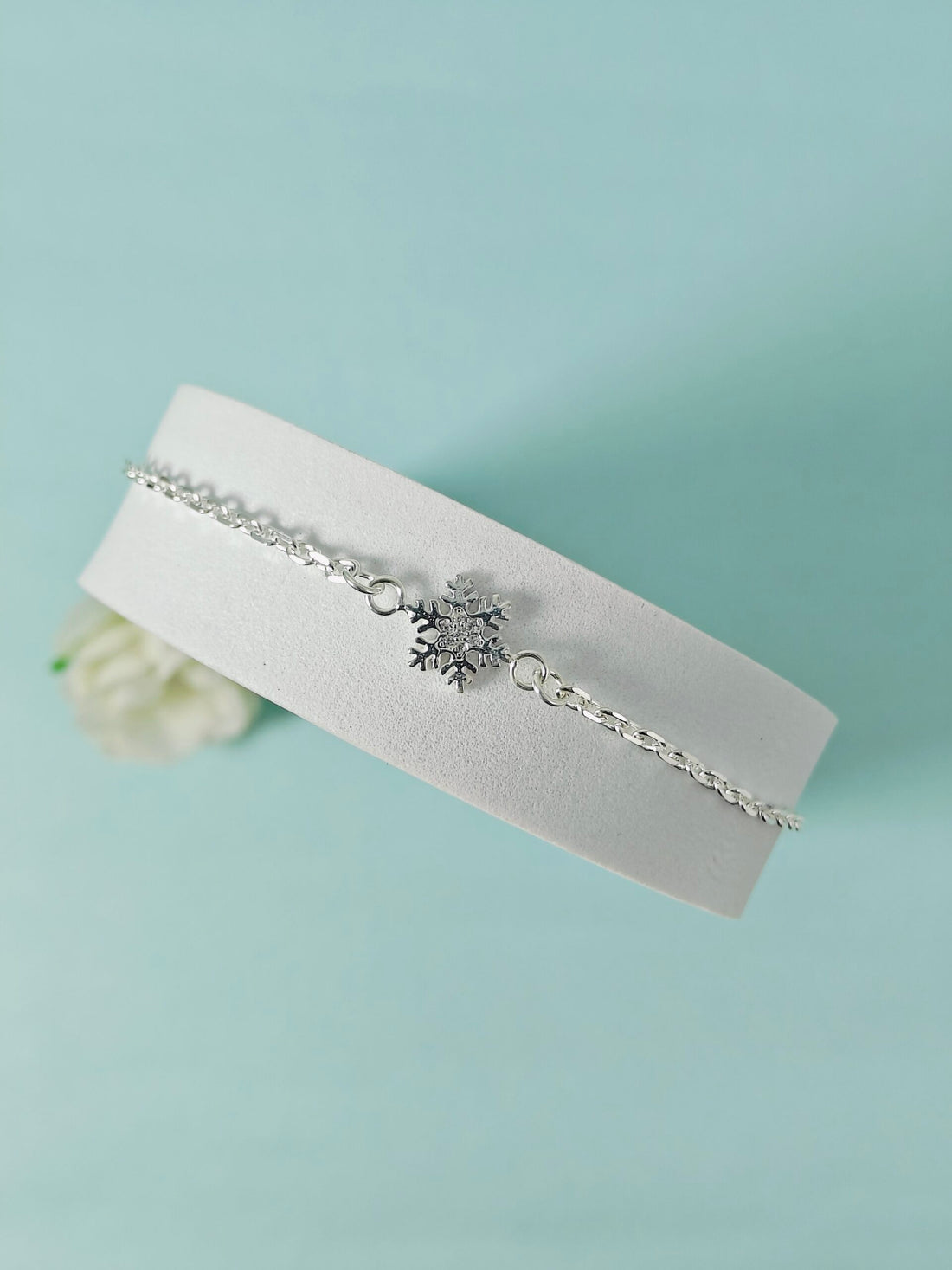Silver bracelet with a snowflake charm on a white cushion against a light blue background