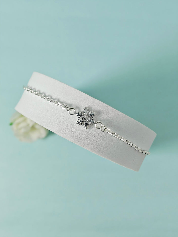 Silver bracelet with a snowflake charm on a white cushion against a light blue background