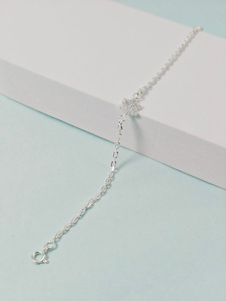 Silver bracelet on a light blue surface with a white box