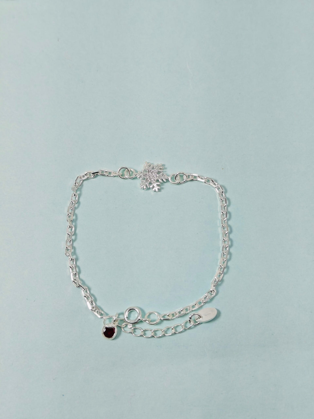 Silver bracelet with heart charm on a light blue background