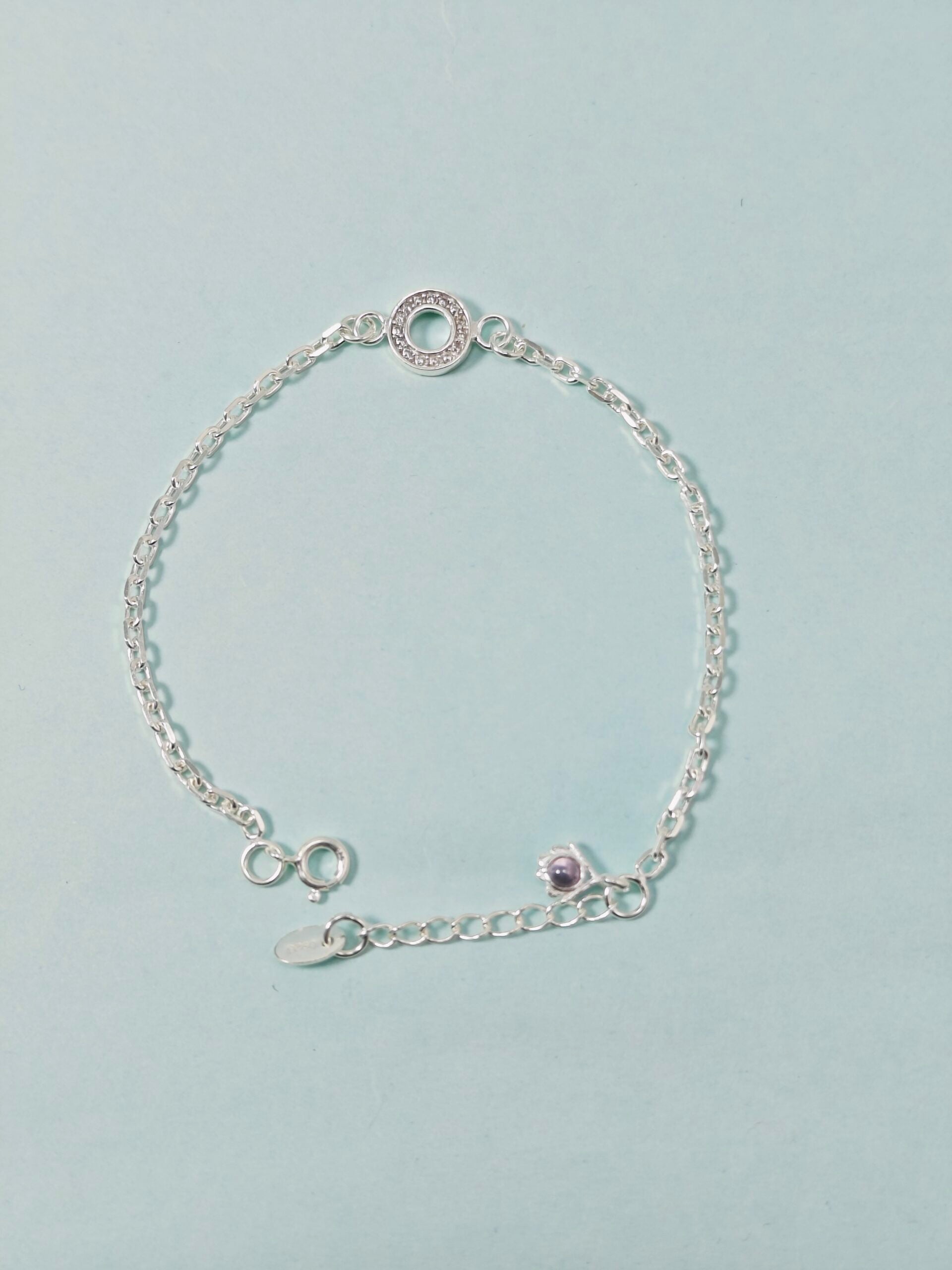 Silver bracelet with a purple gemstone on a light blue background