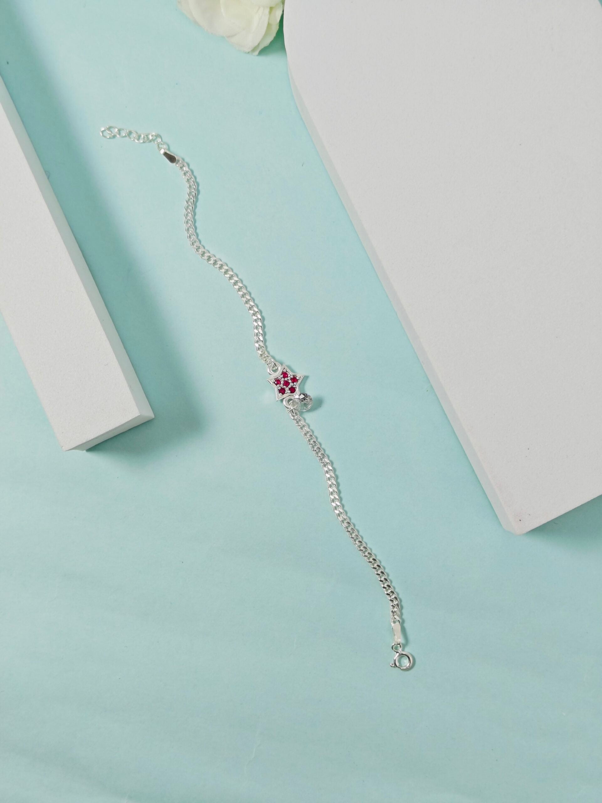 Silver bracelet with a floral charm on a light blue surface