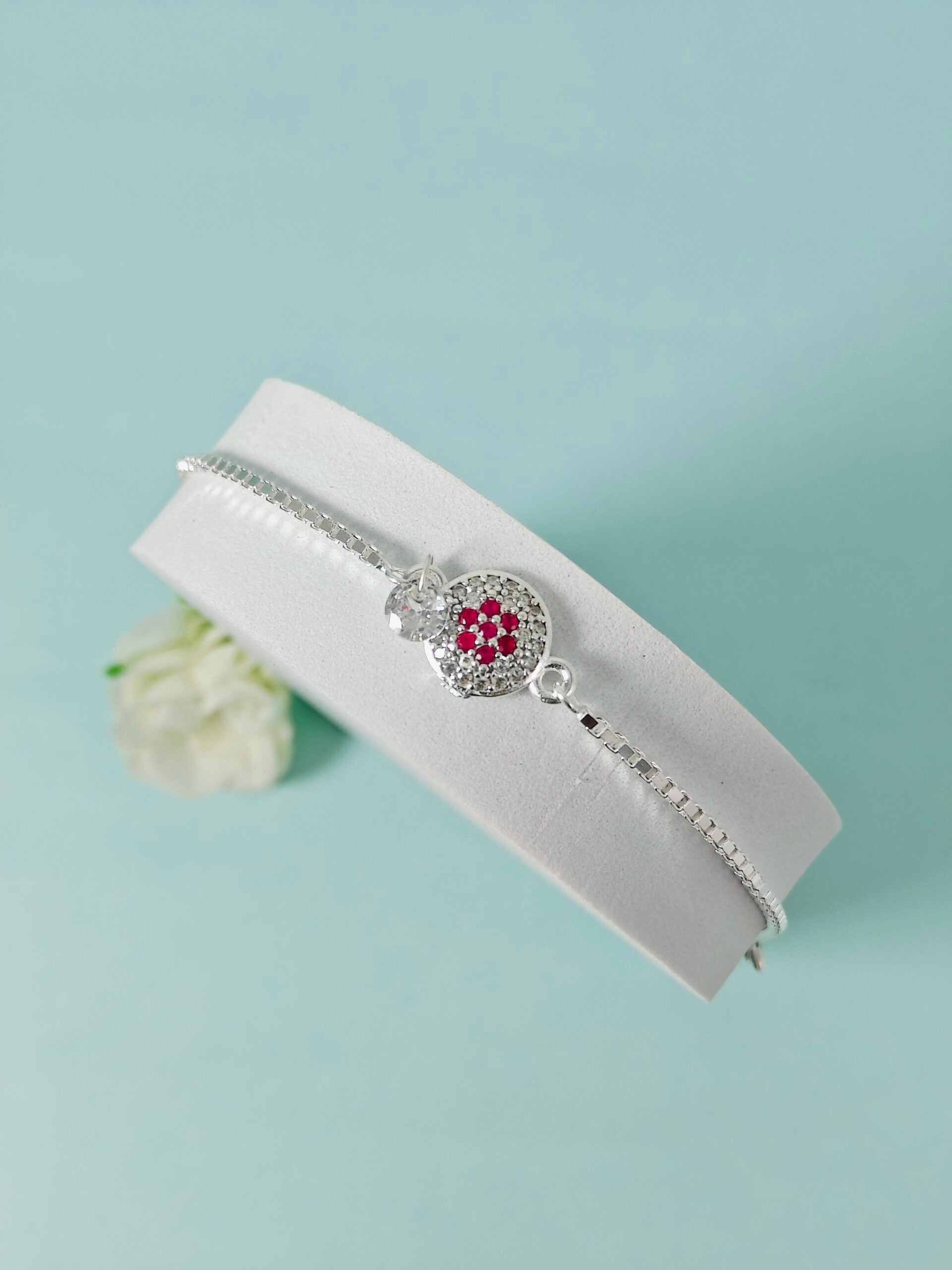 Silver bracelet with a red gemstone on a white box against a light blue background
