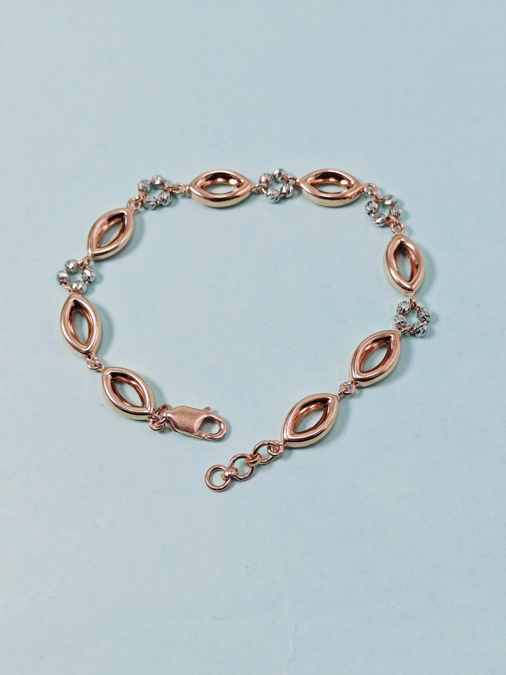 Rose gold bracelet with marquise-shaped links on a light blue background