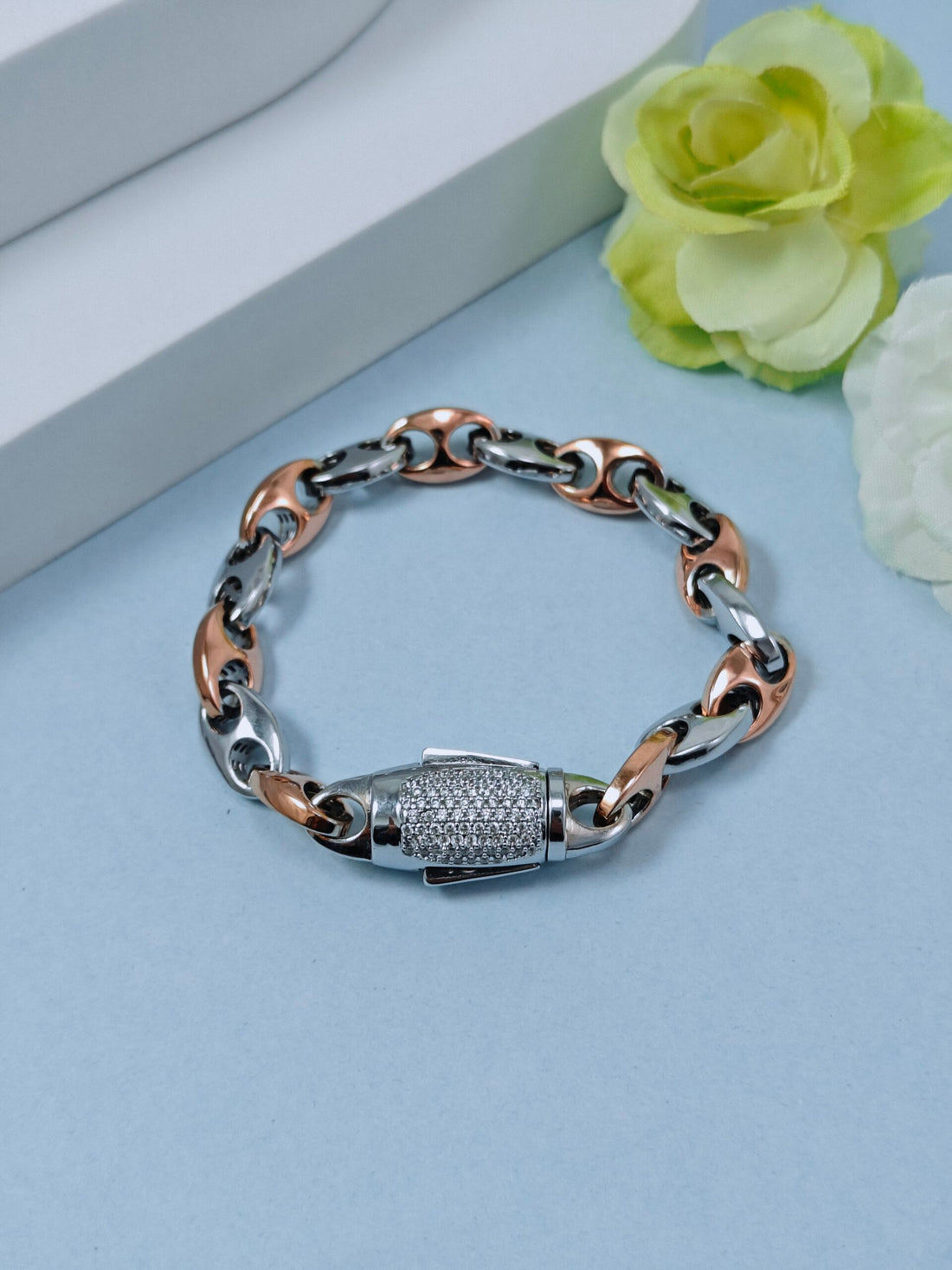 Silver and rose gold chain bracelet on a light blue surface with flowers in the background