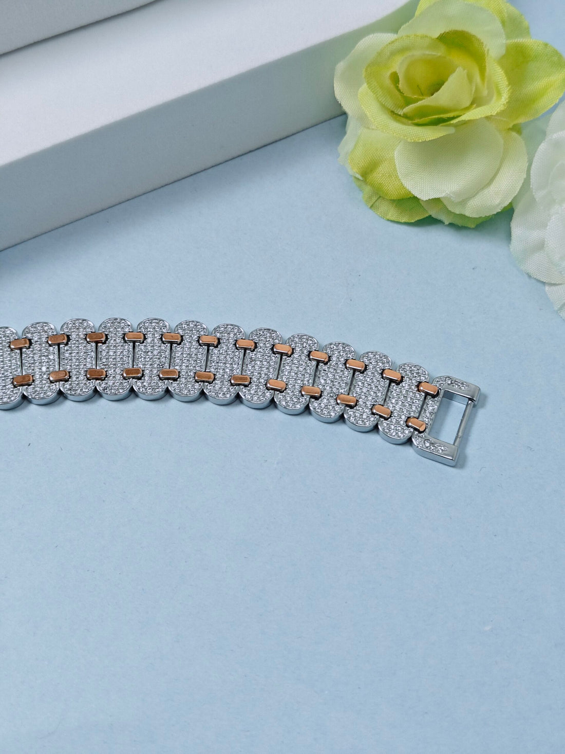 Bracelet with gold and silver chain on a light blue surface with flowers in the background