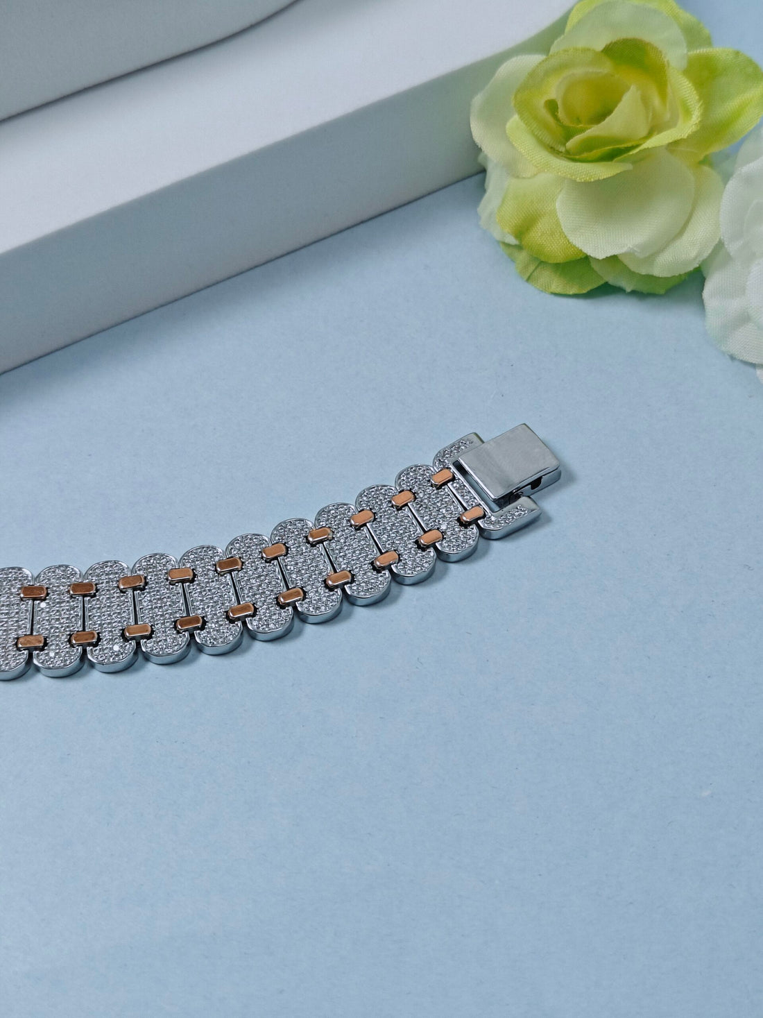 Silver bracelet with brown accents on a light blue surface with a green flower.