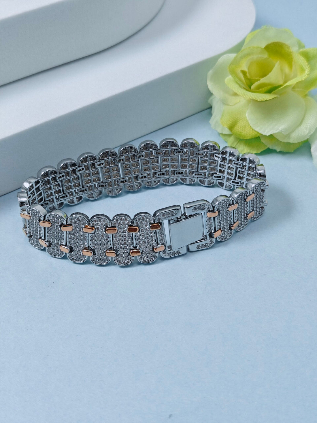 Silver bracelet with rose gold accents on a light blue surface with a yellow flower.