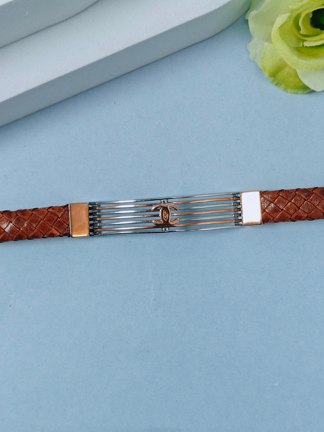 Bracelet with brown woven strap and silver clasp on a light blue surface.