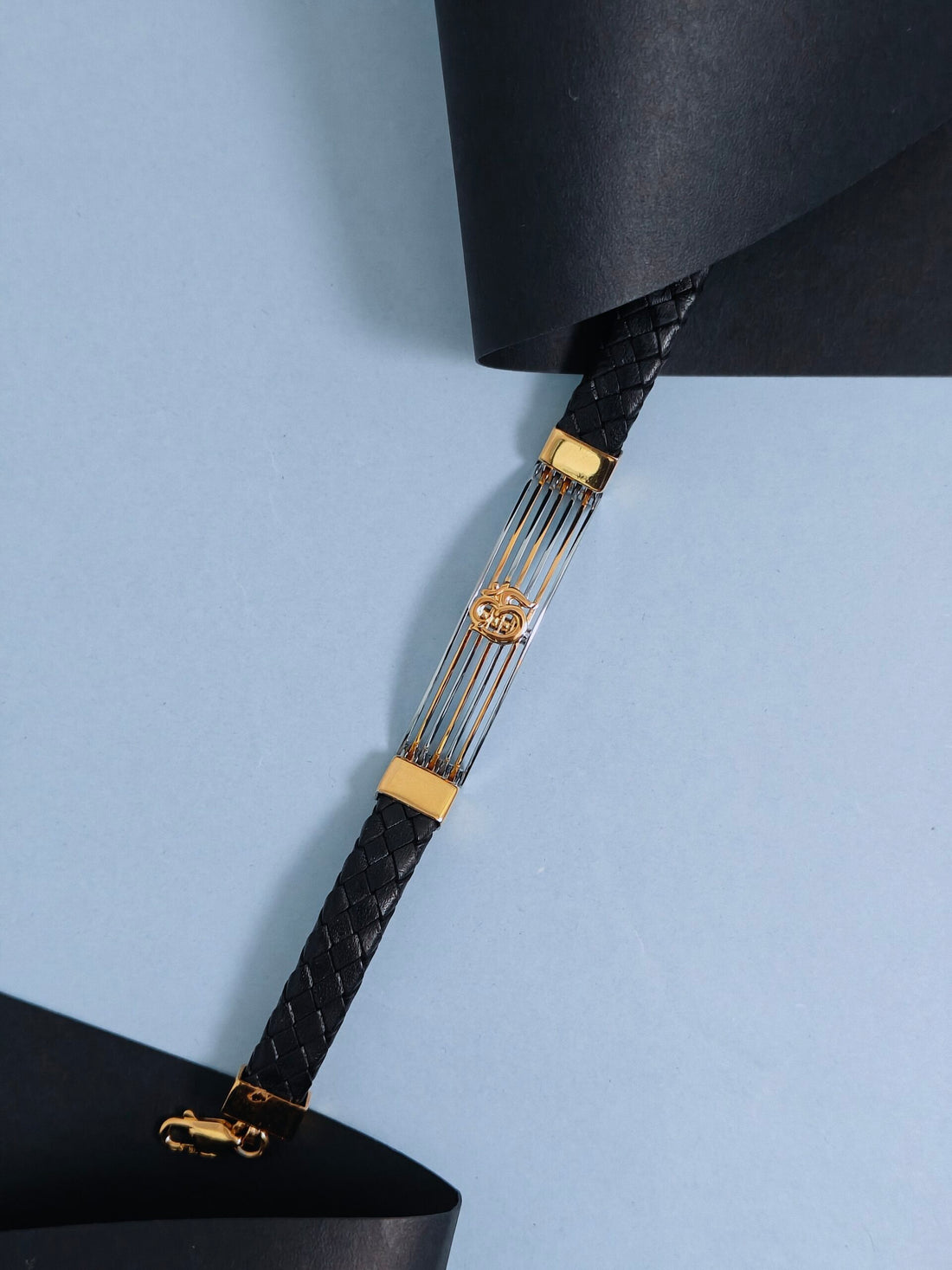 Black textured handbag strap with gold hardware on a light blue background