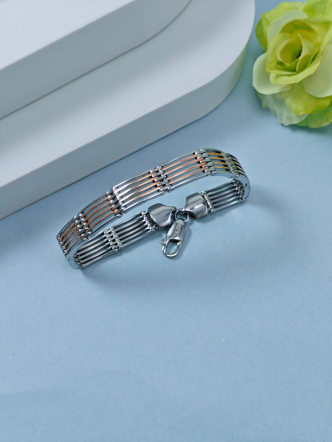 Silver bracelet with a clasp on a light blue surface with a yellow flower.