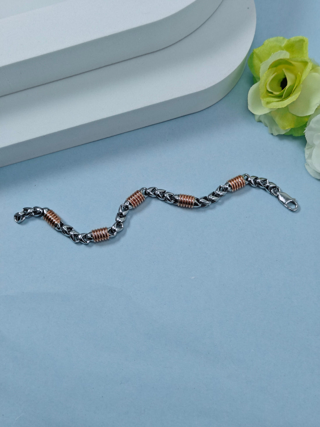 Bracelet with braided design on a light blue surface with a white flower.