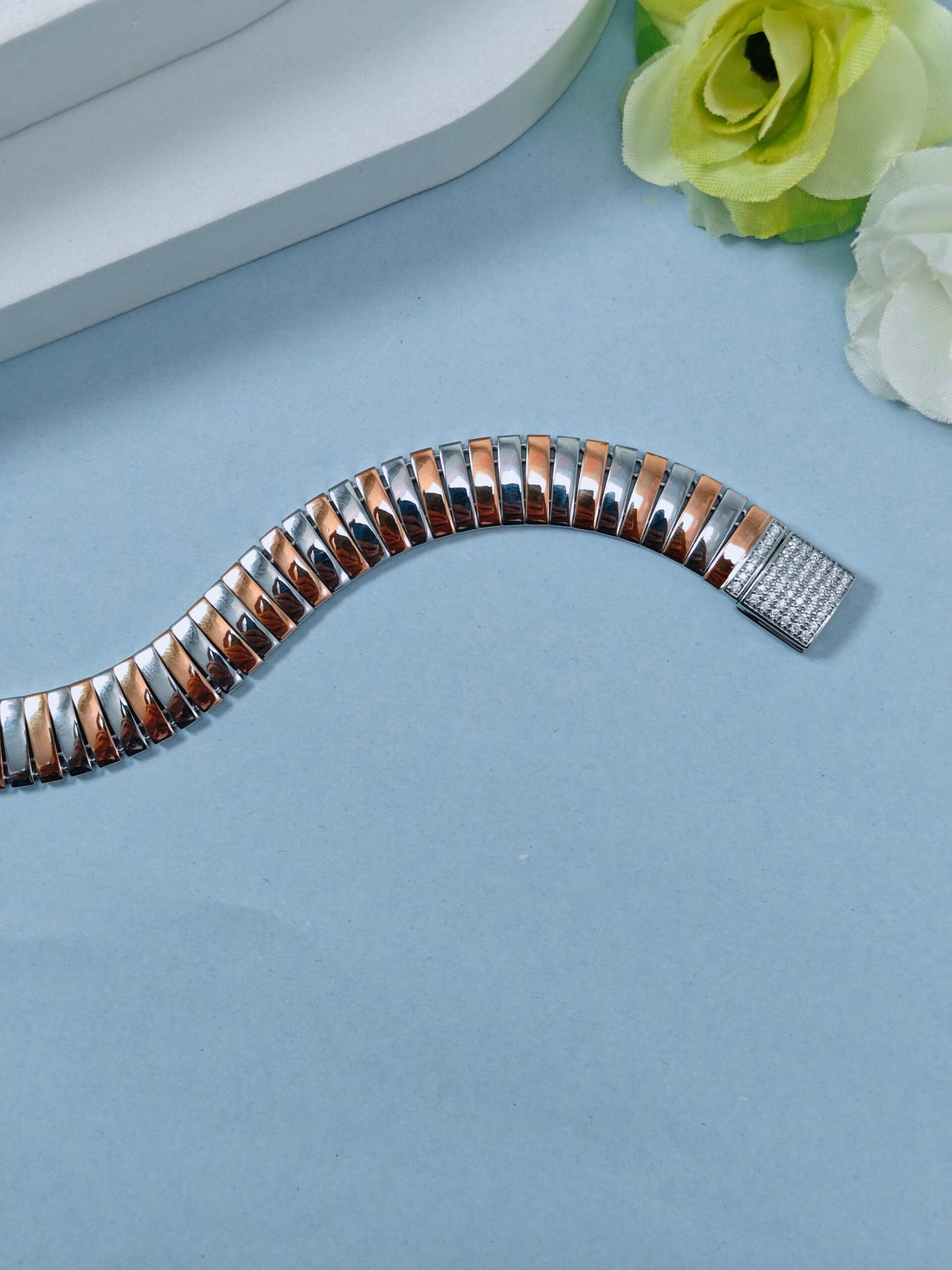 Silver and rose gold watch band on a light blue surface with flowers in the background