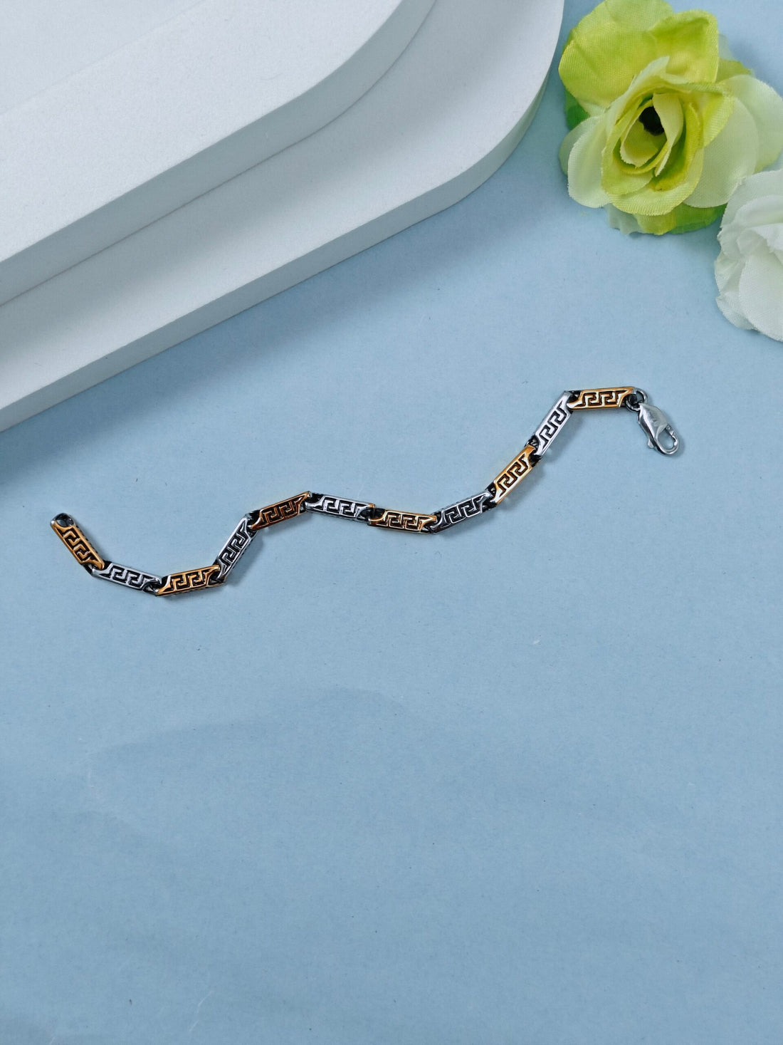 Gold and silver chain bracelet on a light blue surface with flowers in the background