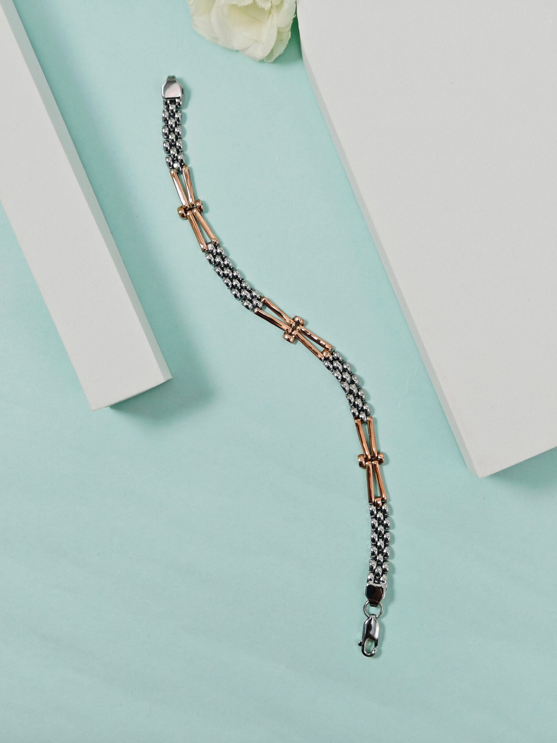 Two-tone bracelet on a light blue surface with a white flower in the background