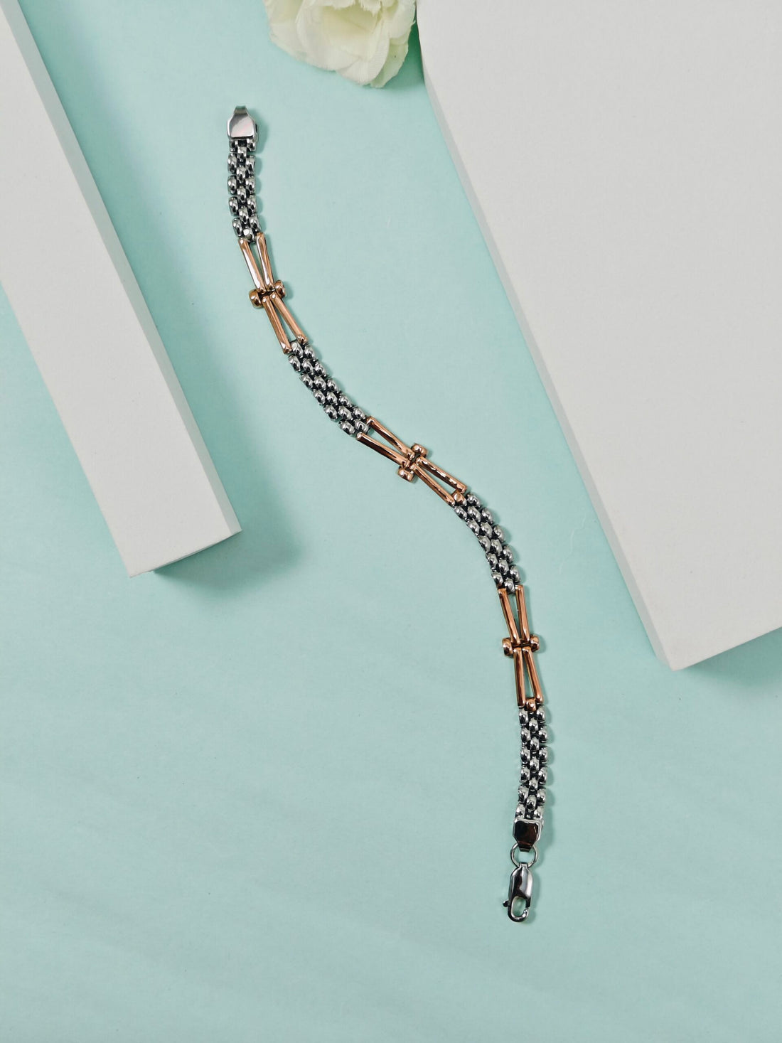 Two-tone bracelet on a light blue surface with a white flower in the background