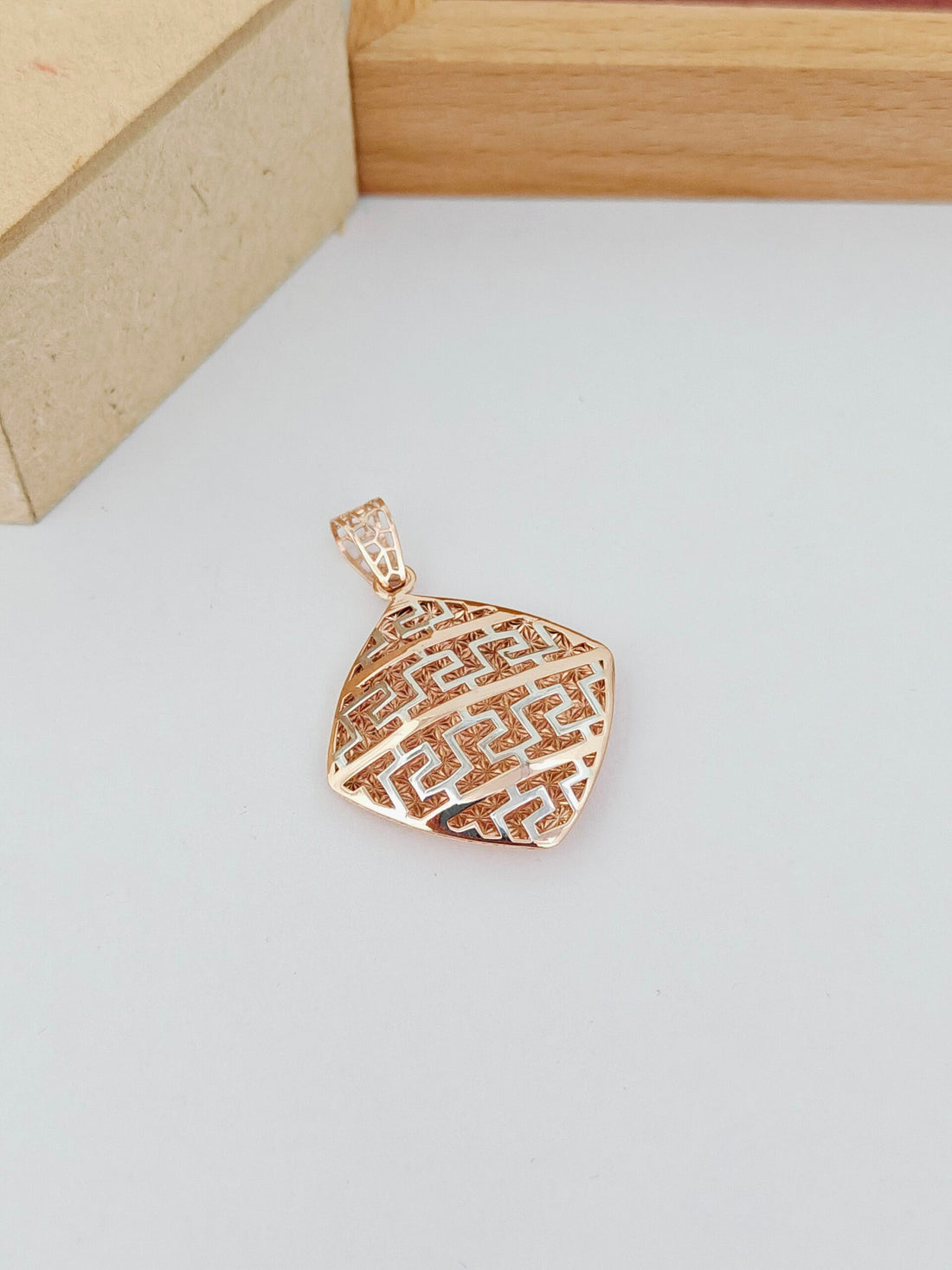 Gold pendant on a light gray surface with a wooden box in the background