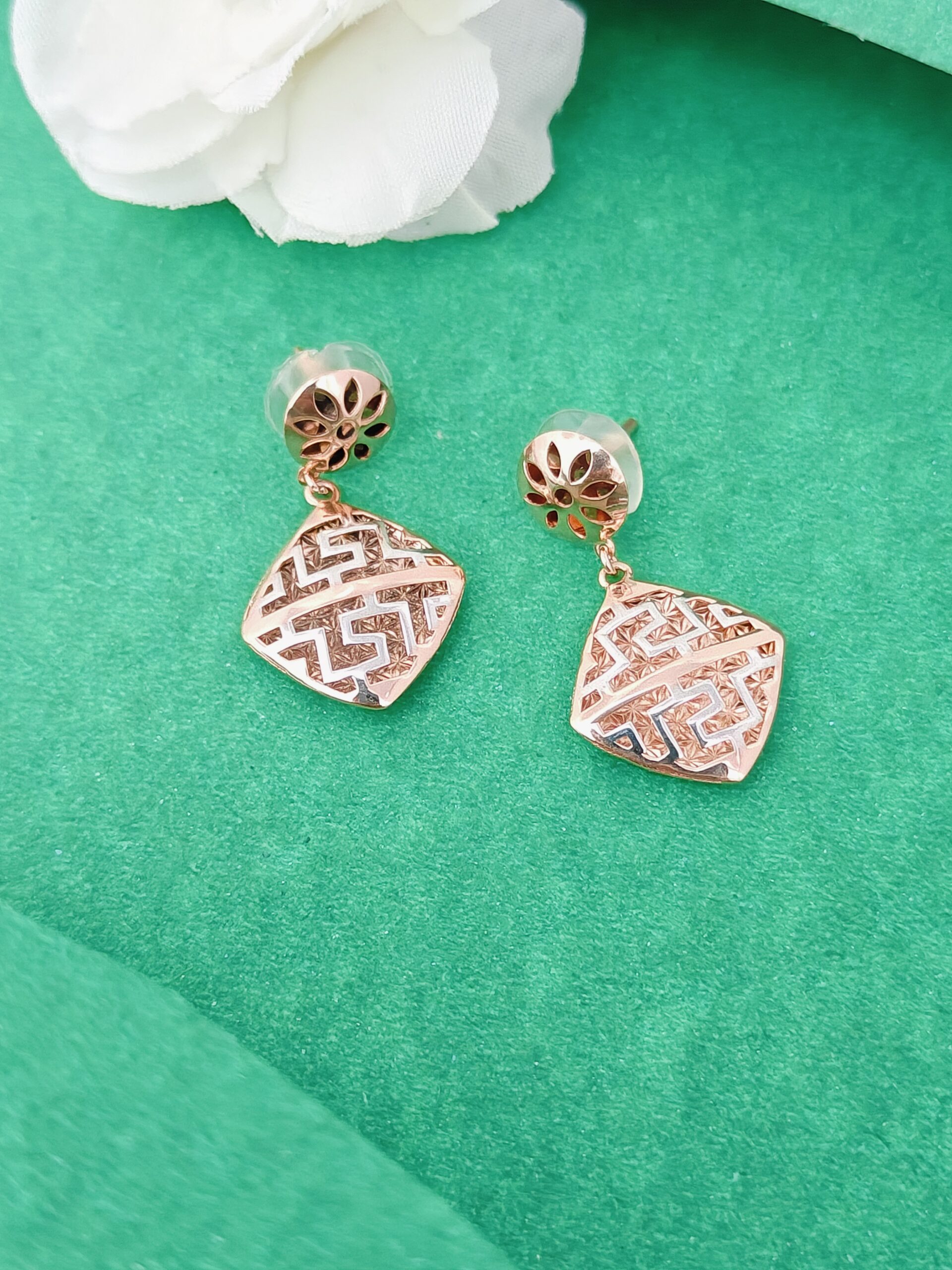 Rose gold earrings on a green surface with white flowers in the background