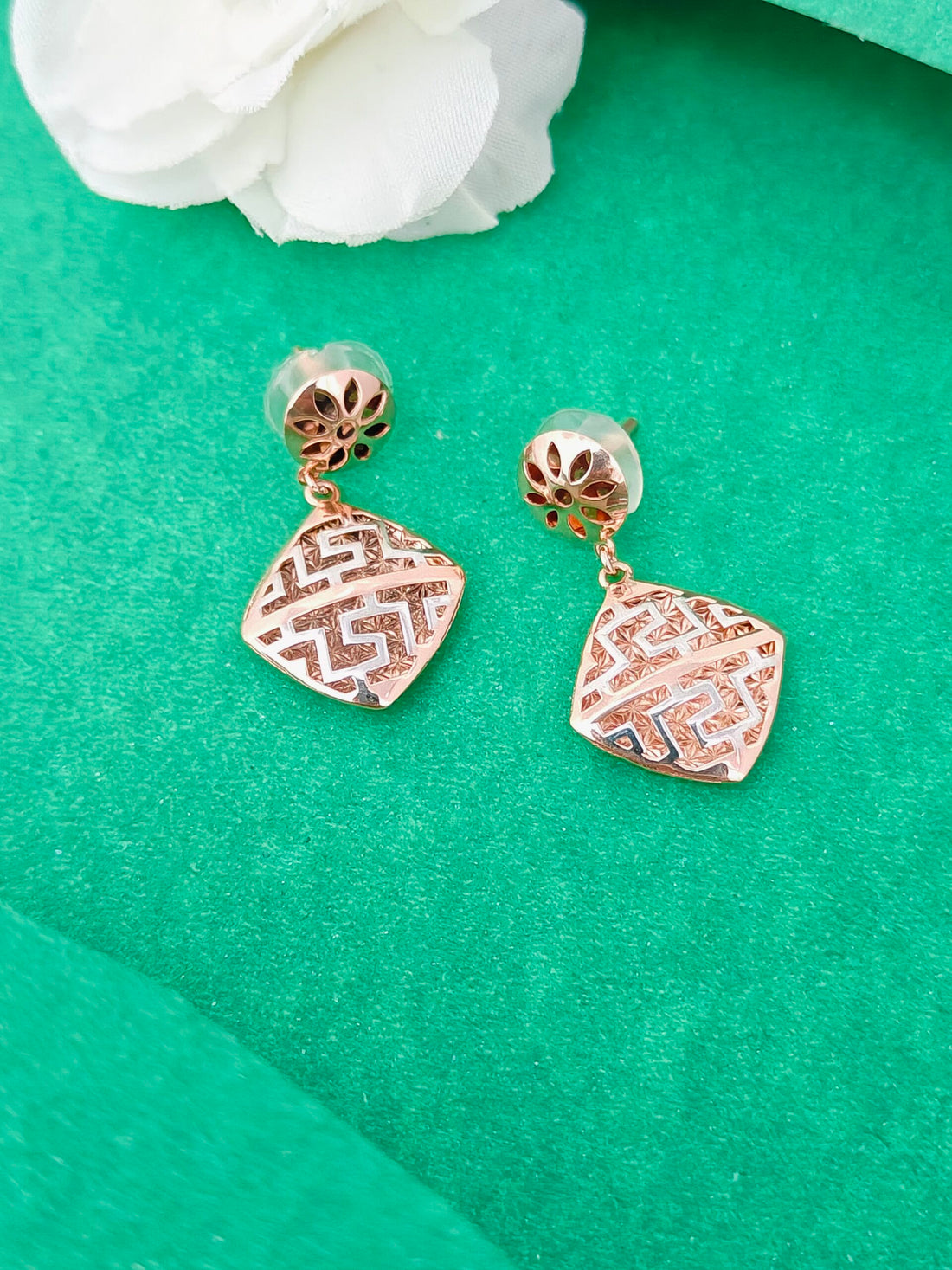 Rose gold earrings on a green surface with white flowers in the background