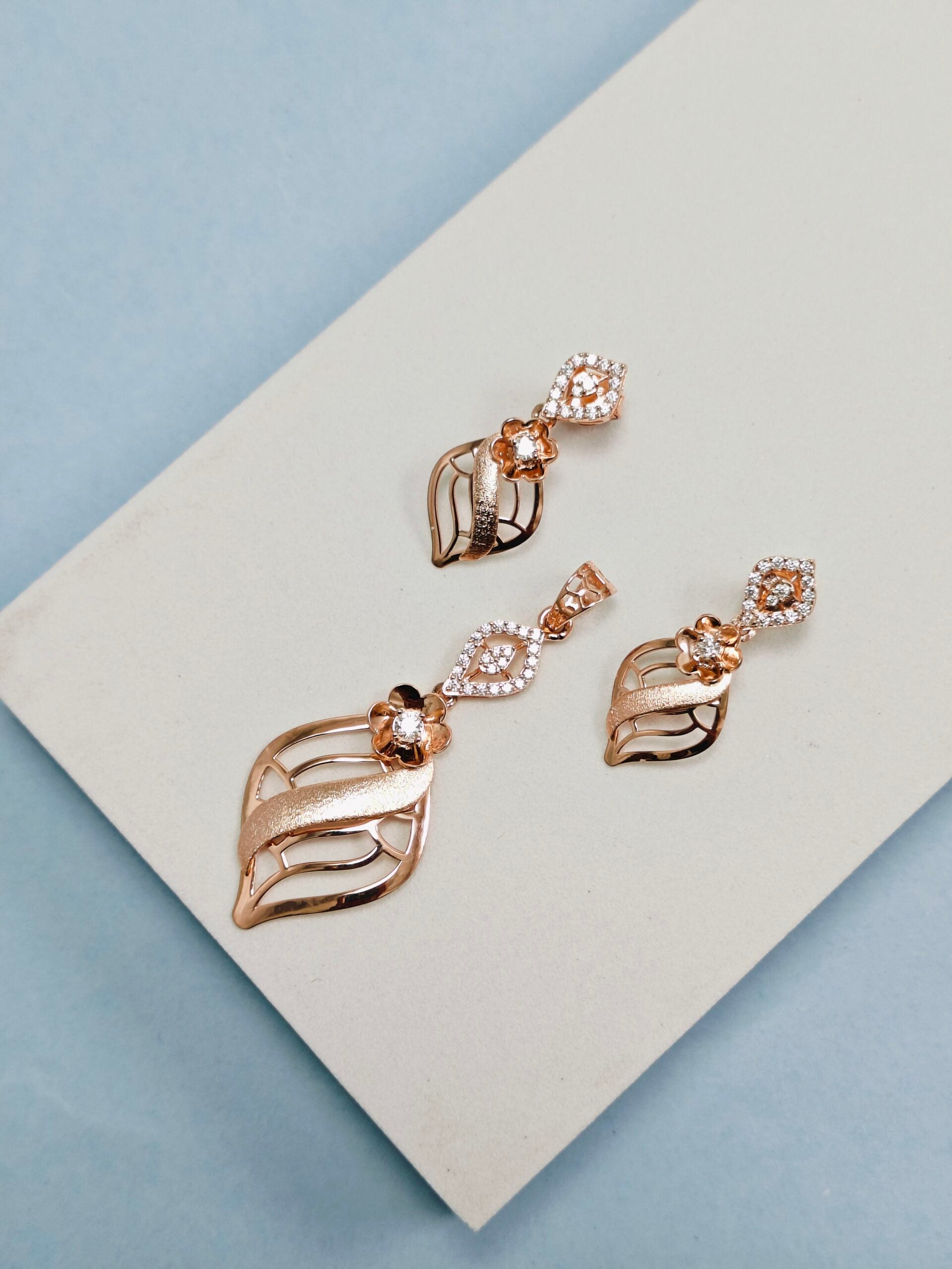Rose gold earrings with leaf design on a white card against a light blue background