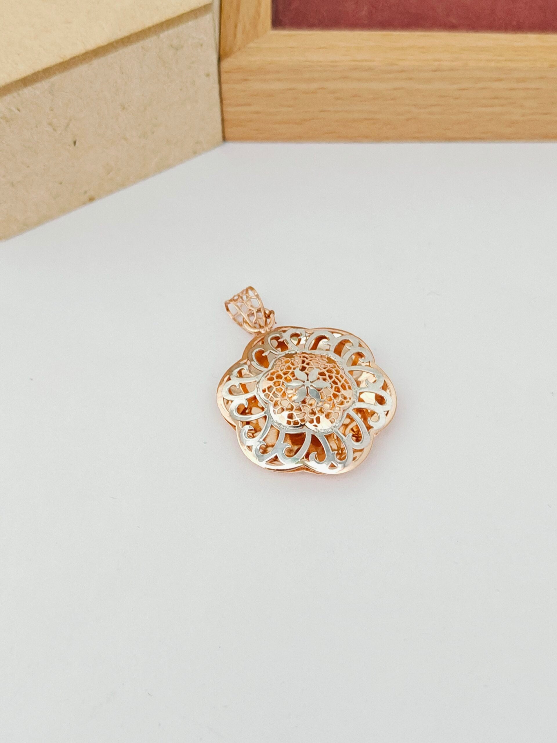 Gold floral pendant on a light gray surface with a wooden frame in the background