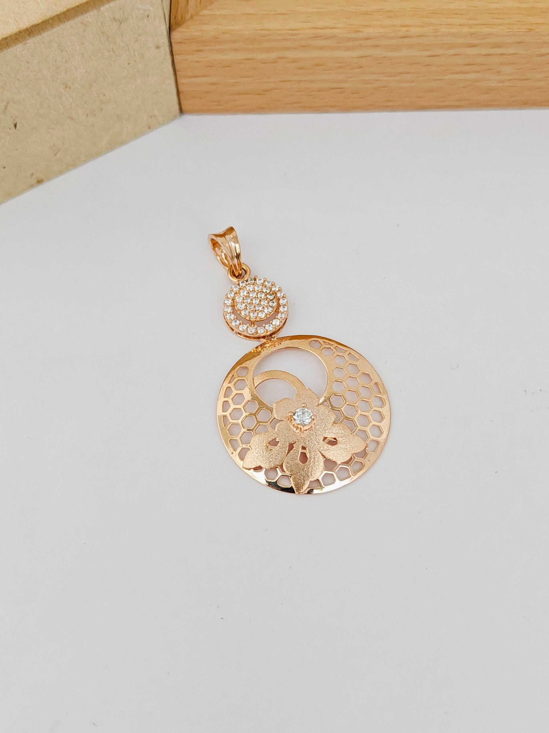 Gold pendant on a light gray surface with a wooden box in the background