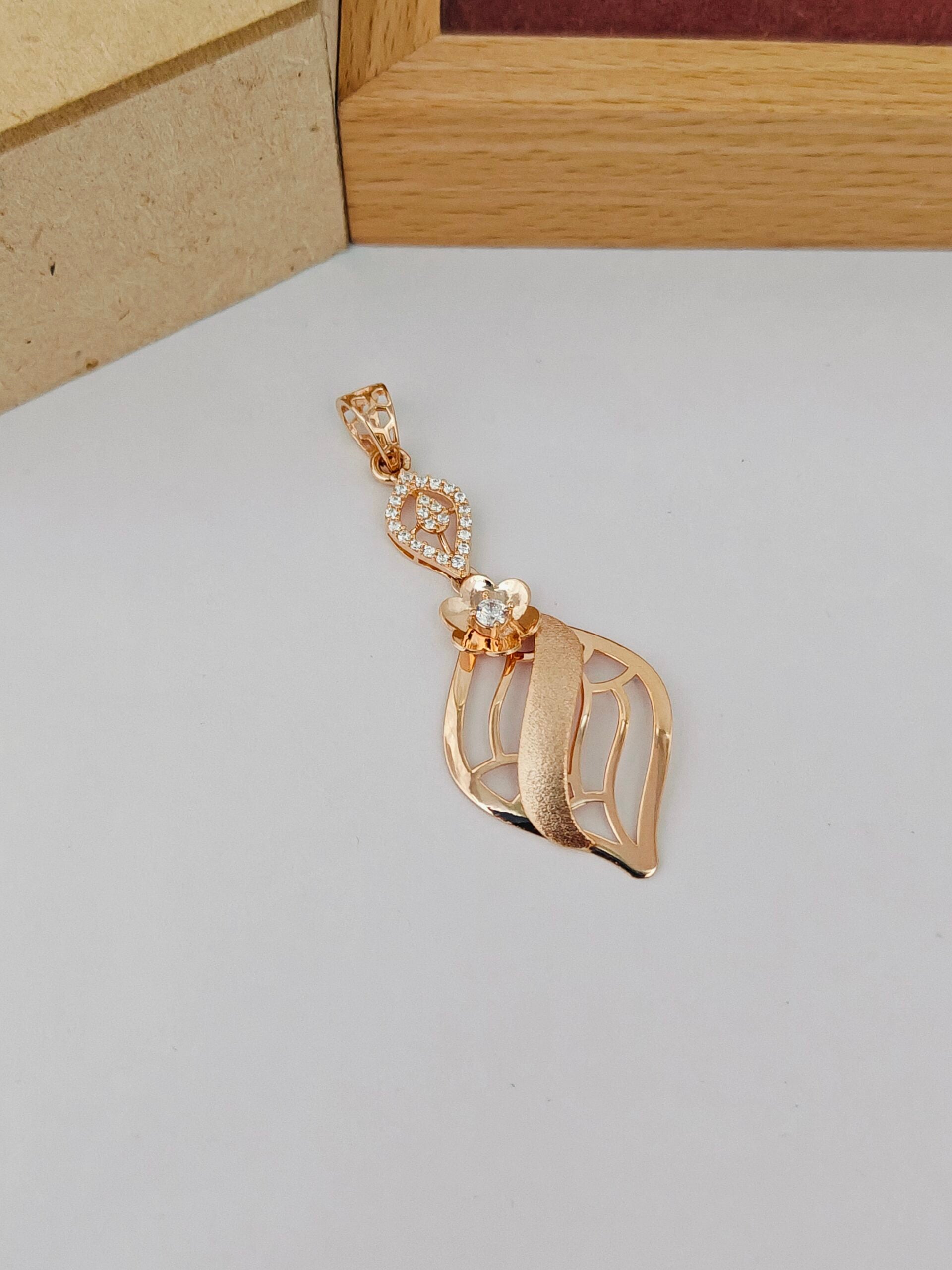 Gold pendant with leaf design on a light gray surface