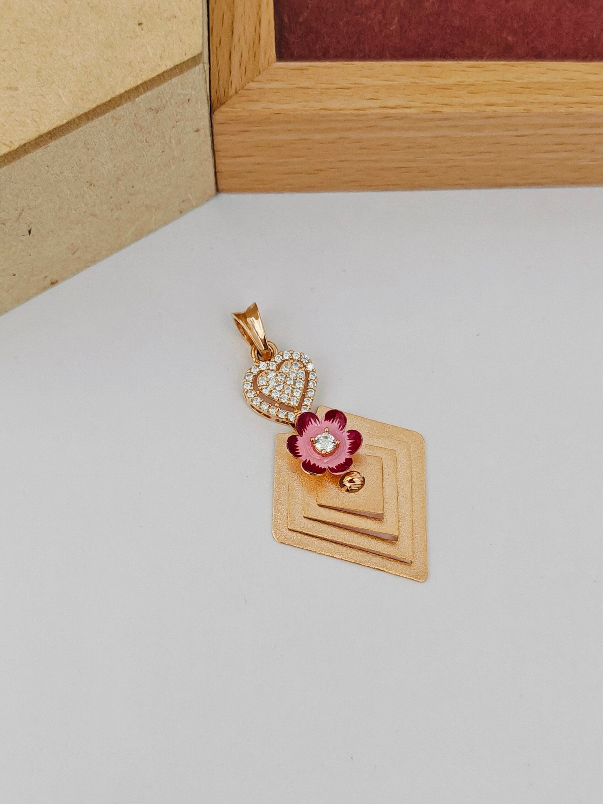 Gold pendant with a pink flower design on a wooden stand