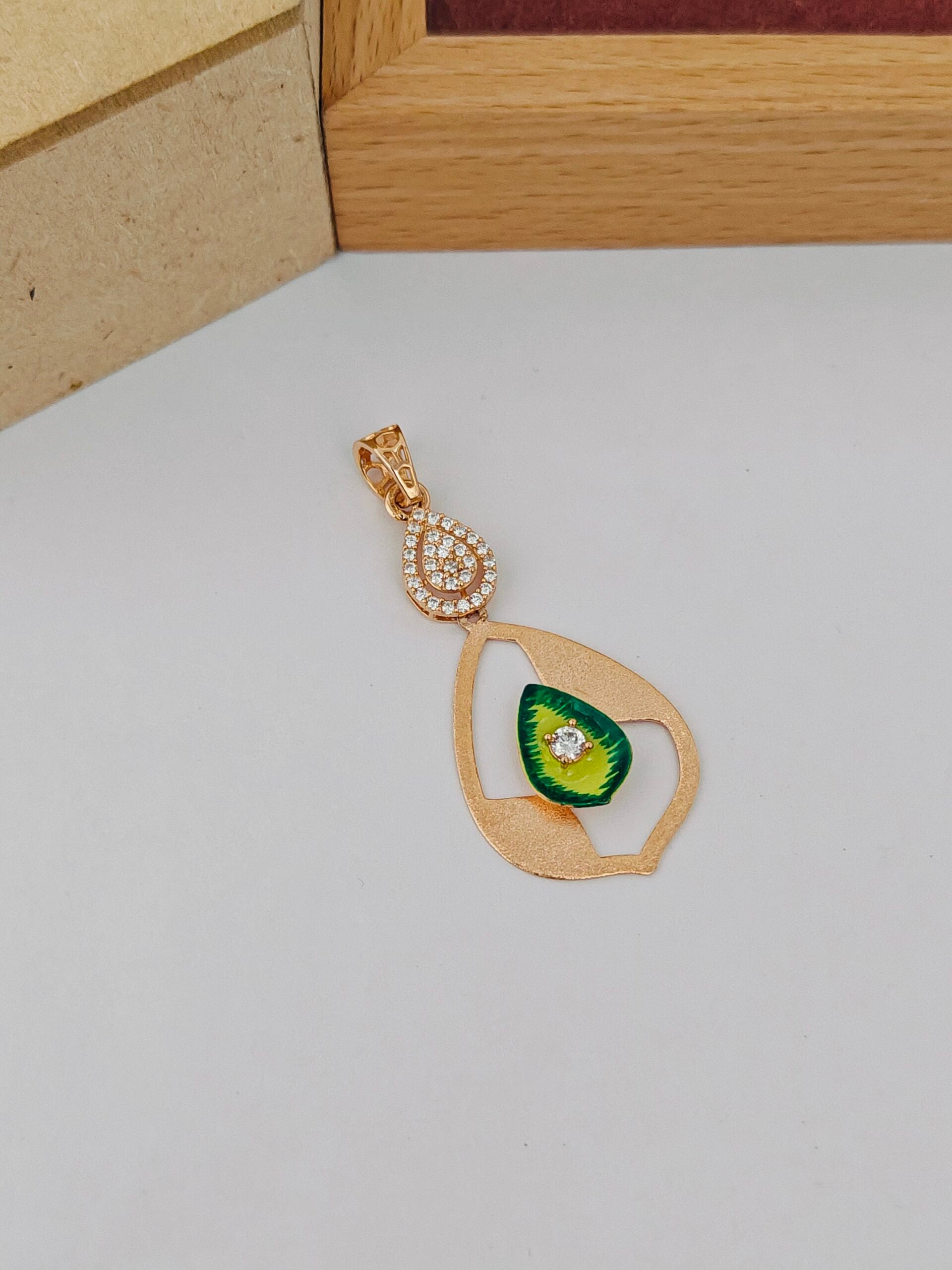 Gold pendant with green gemstone on a light gray surface