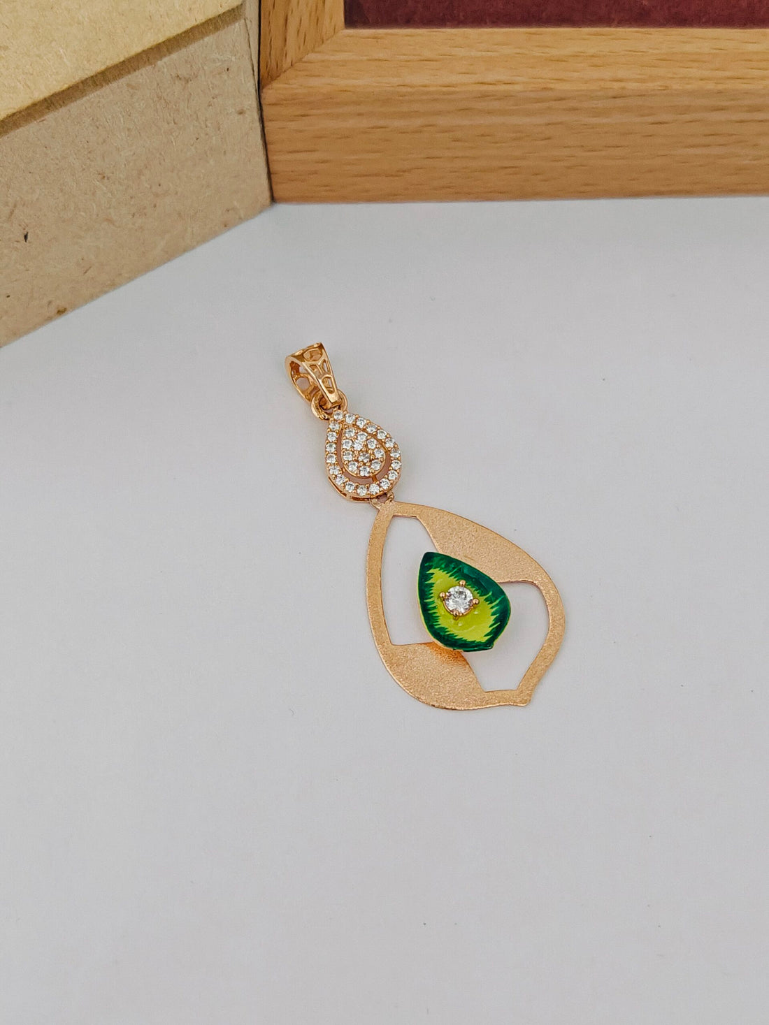 Gold pendant with green gemstone on a light gray surface