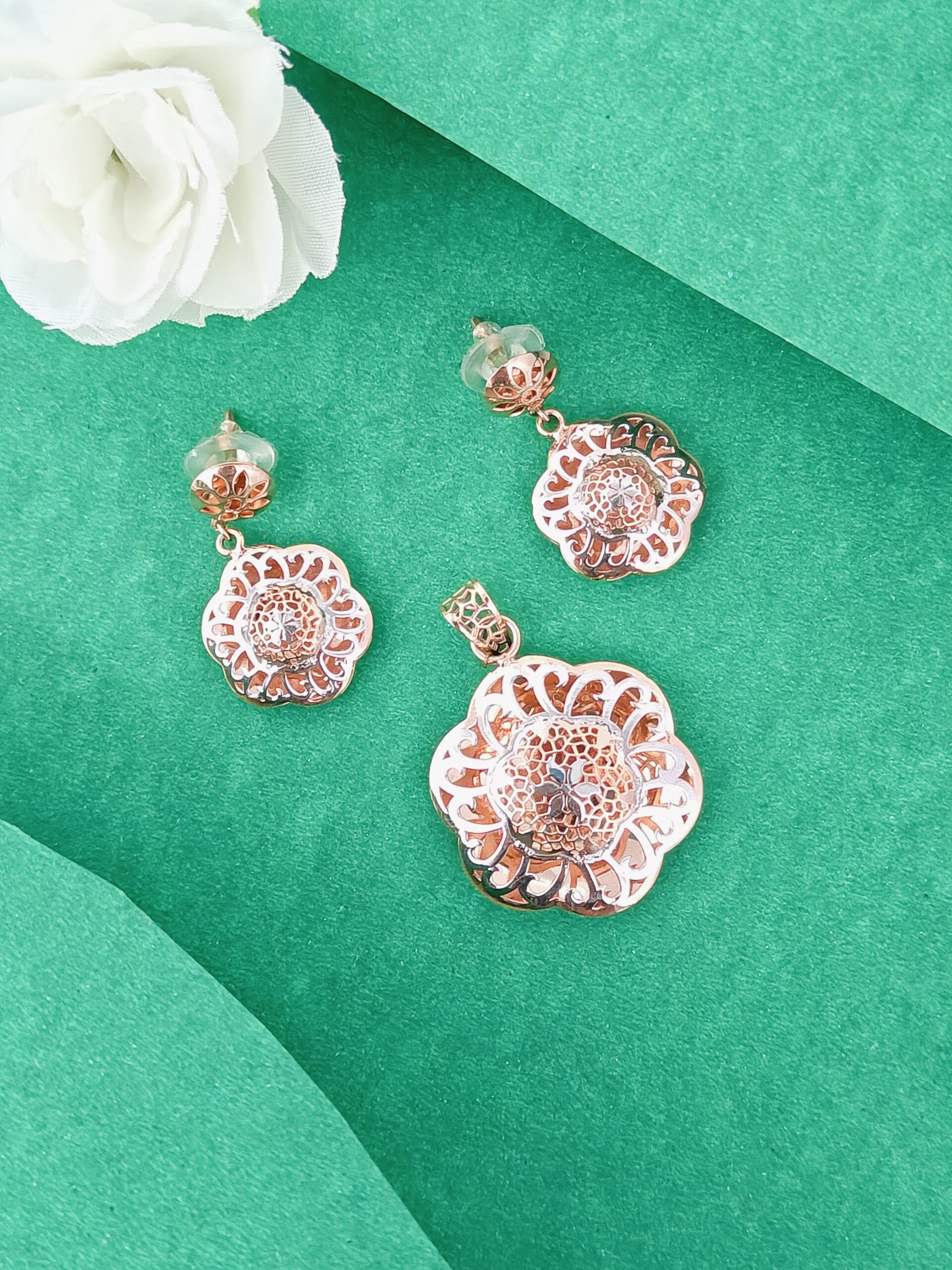 Rose gold floral earrings on a green background with a white flower.