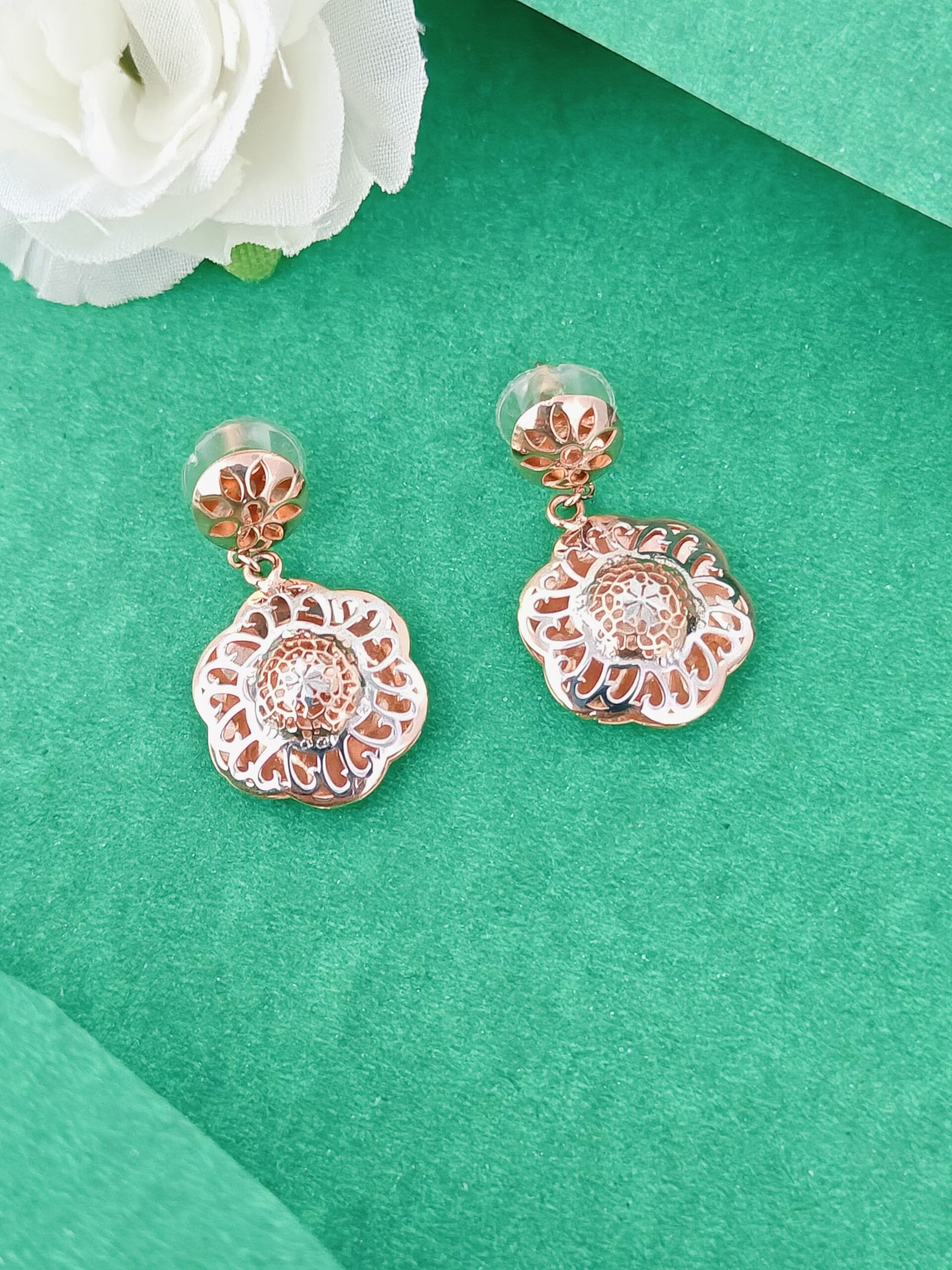 Rose gold floral earrings on a green background with a white flower.