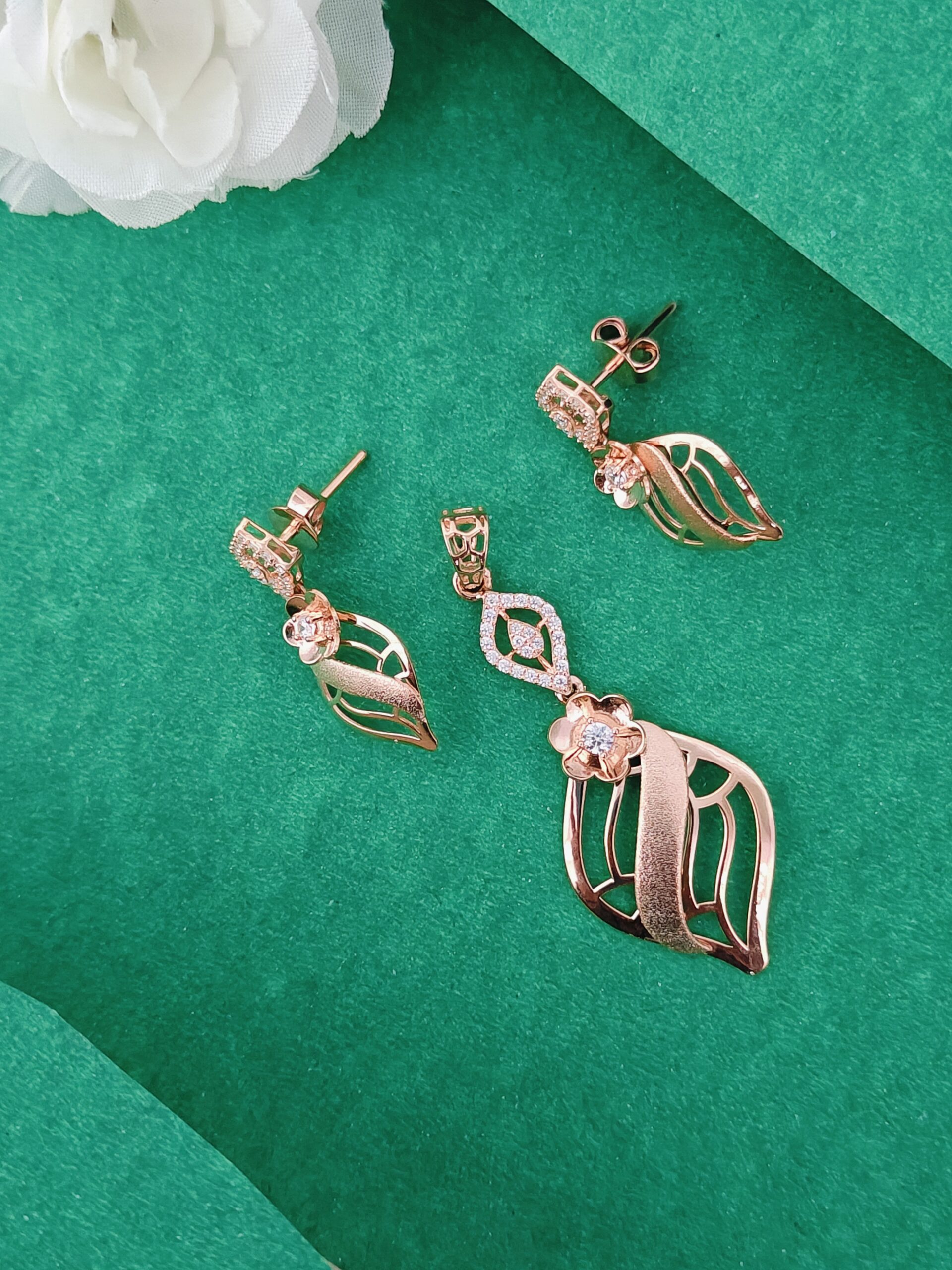 Rose gold leaf-shaped earrings on a green surface with white flowers.