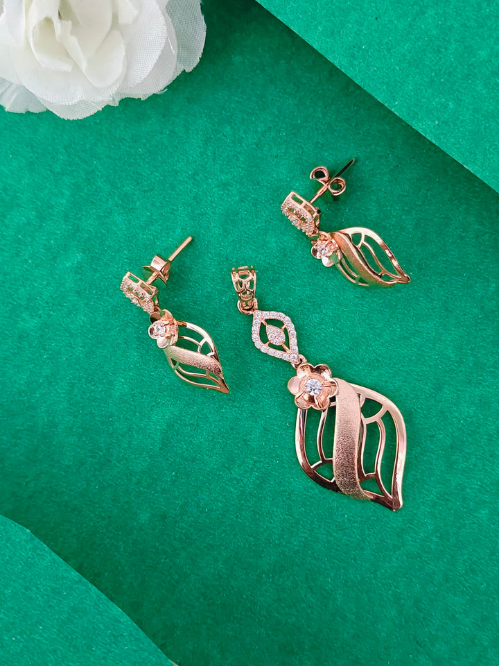 Rose gold leaf-shaped earrings on a green surface with white flowers.