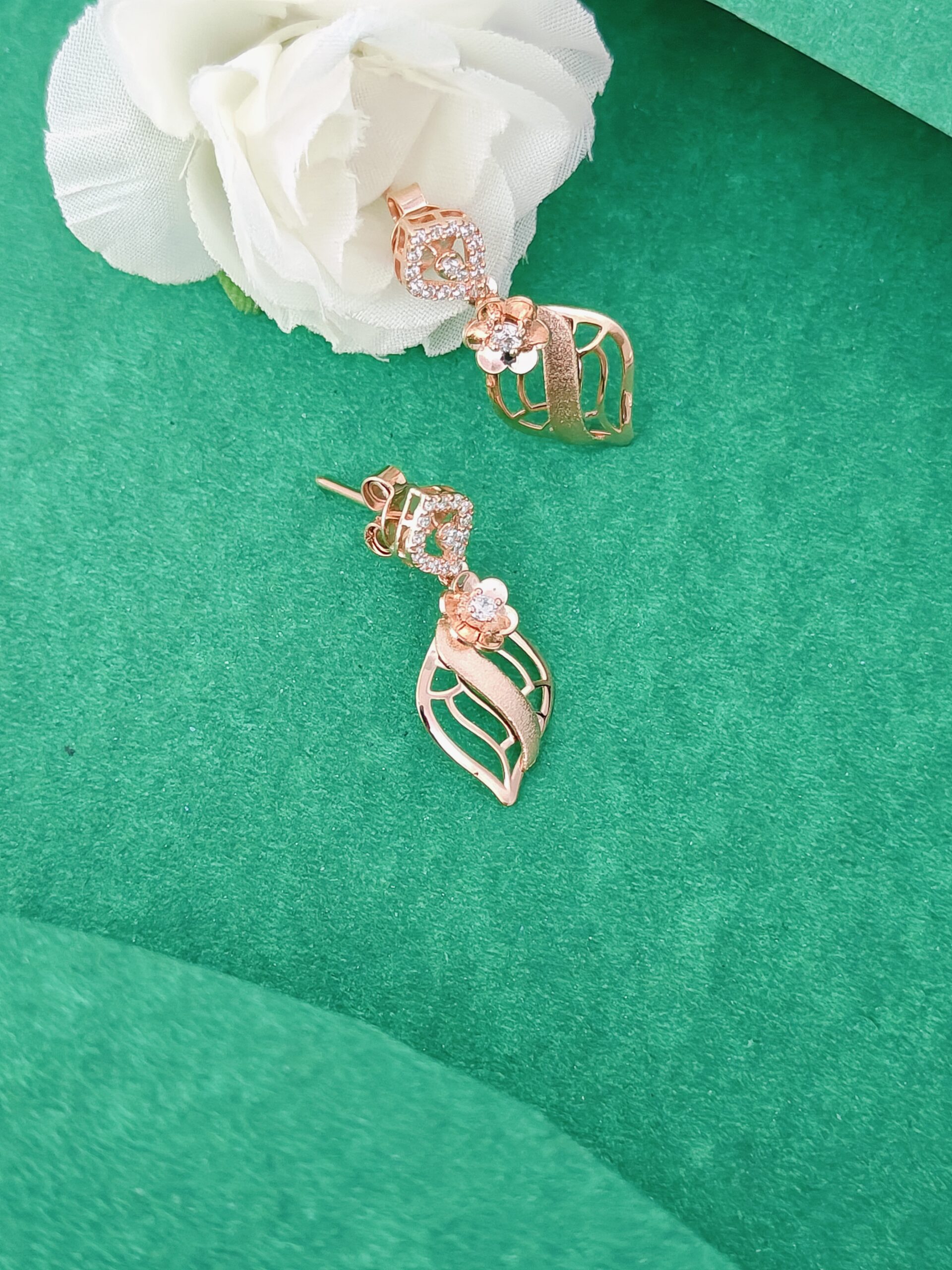 Rose gold earrings with diamond accents on a green surface with a white flower.