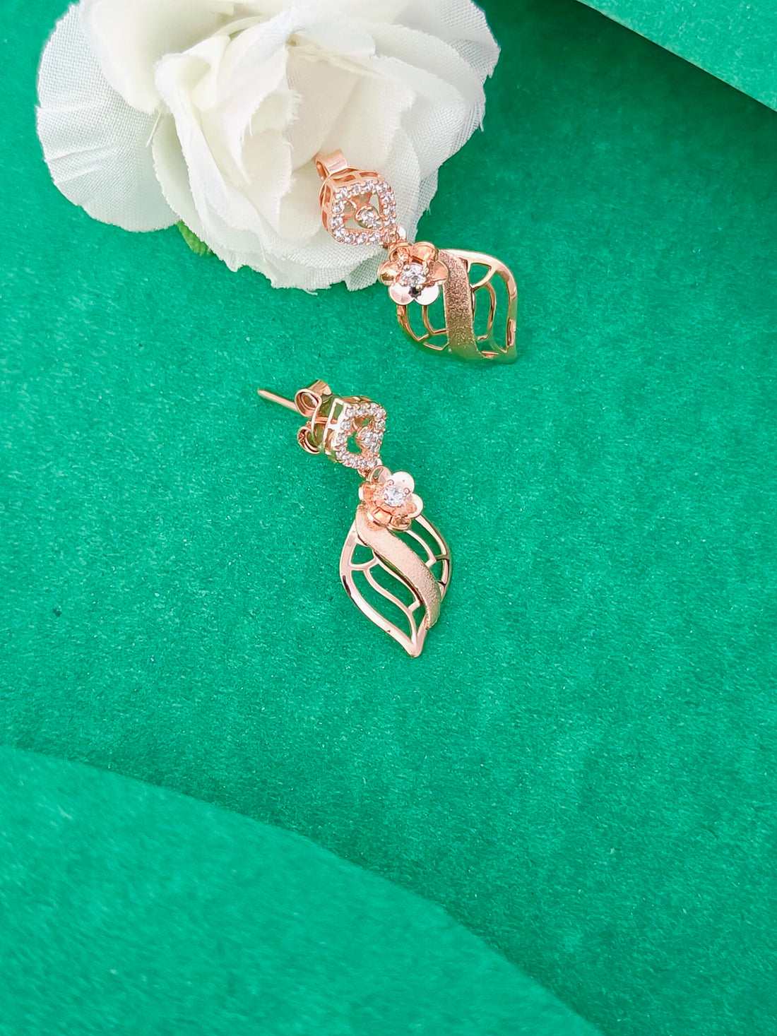 Rose gold earrings with diamond accents on a green surface with a white flower.