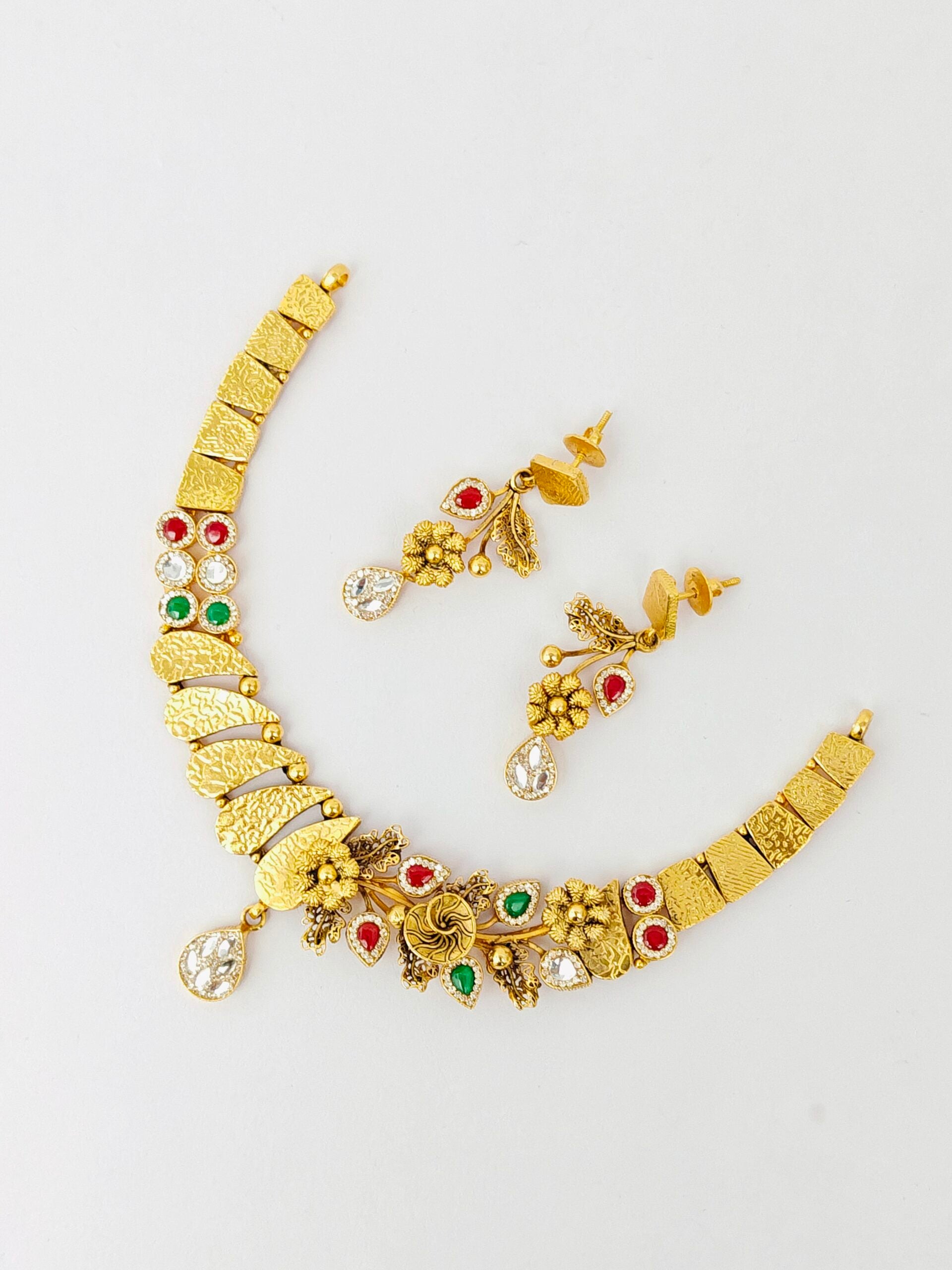 Gold necklace with red and green gemstones on a white background