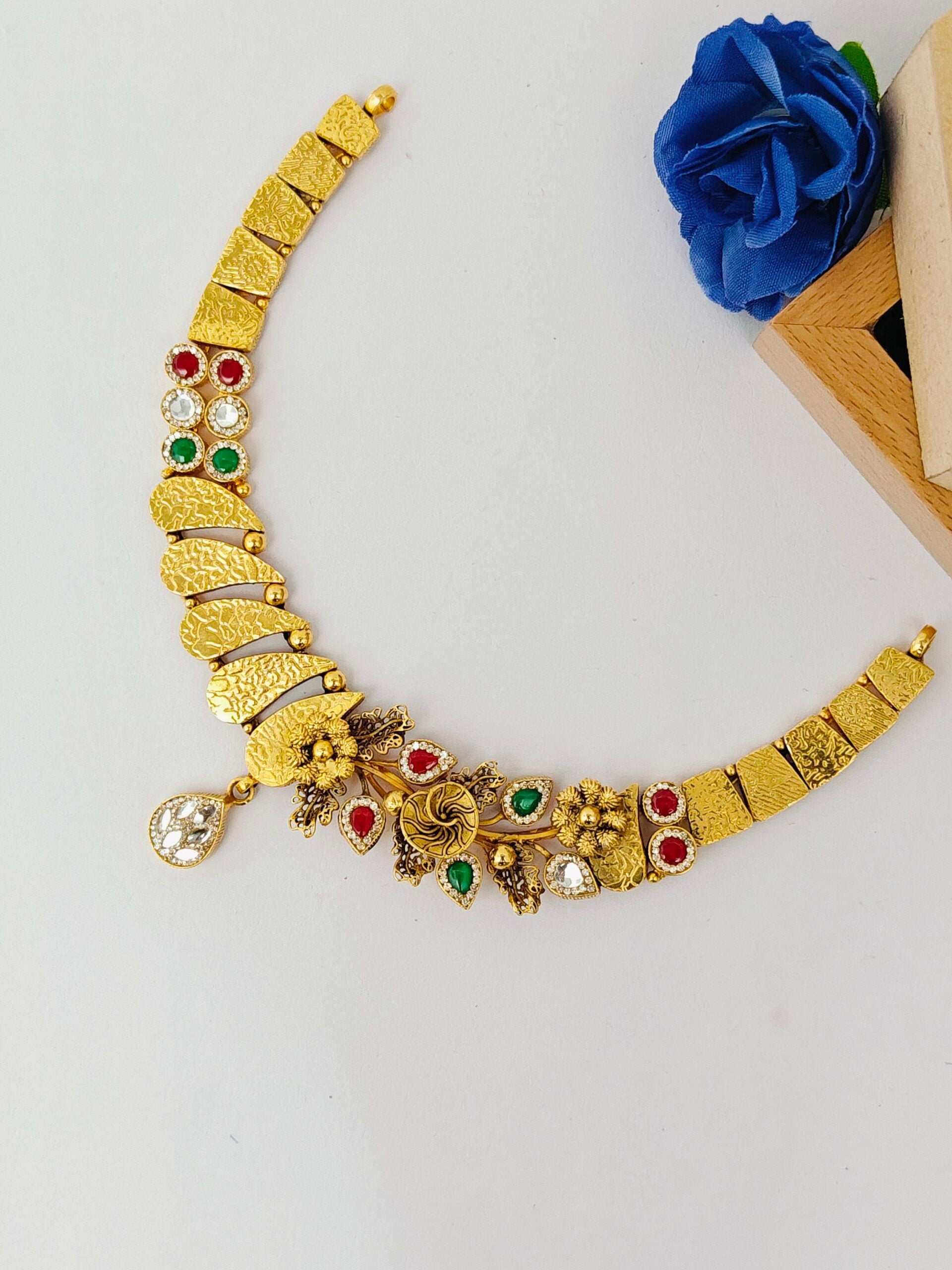 Gold necklace with red and green gemstones on a white background