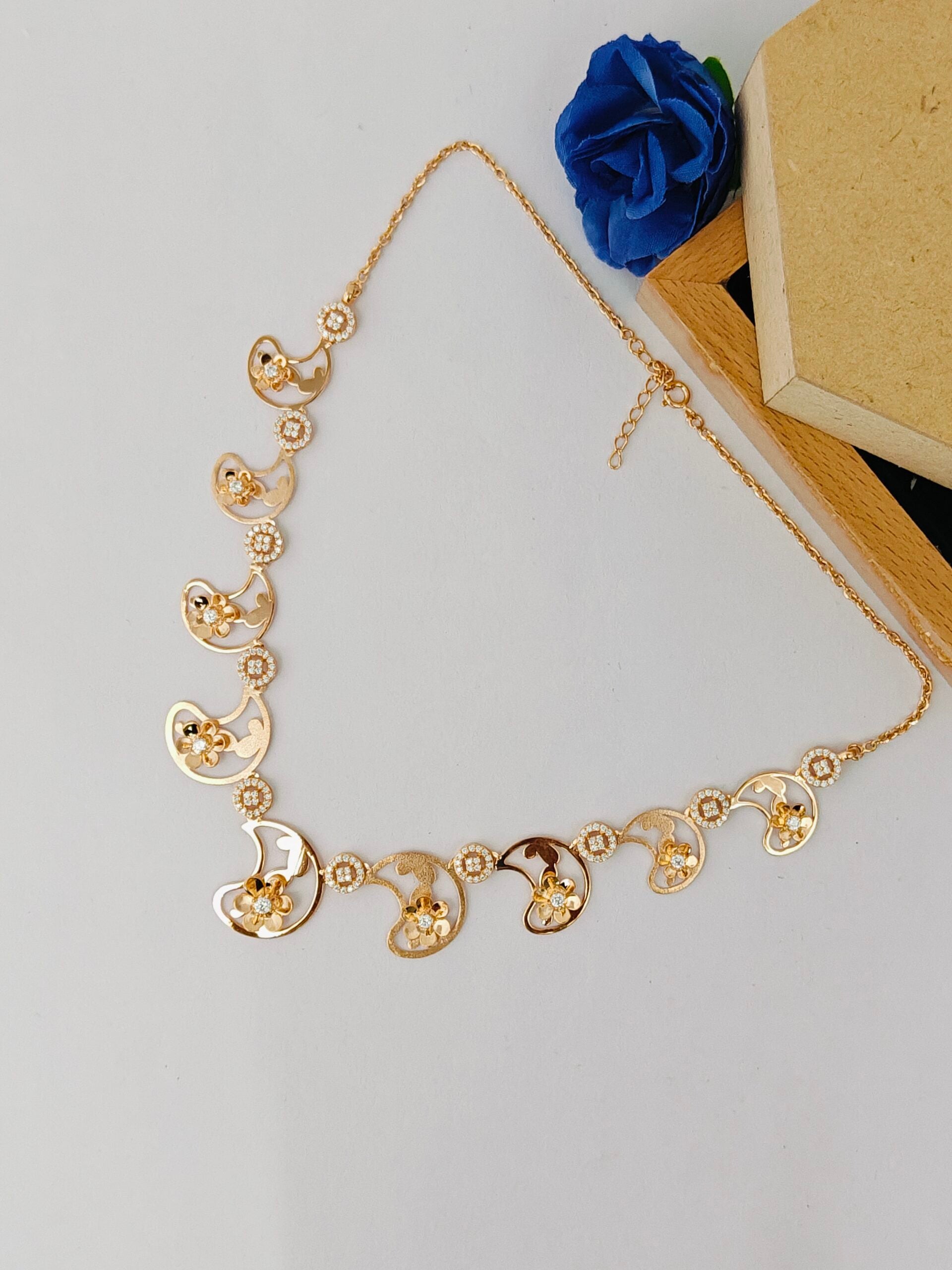 Gold necklace on a light gray background with a blue flower and beige box.