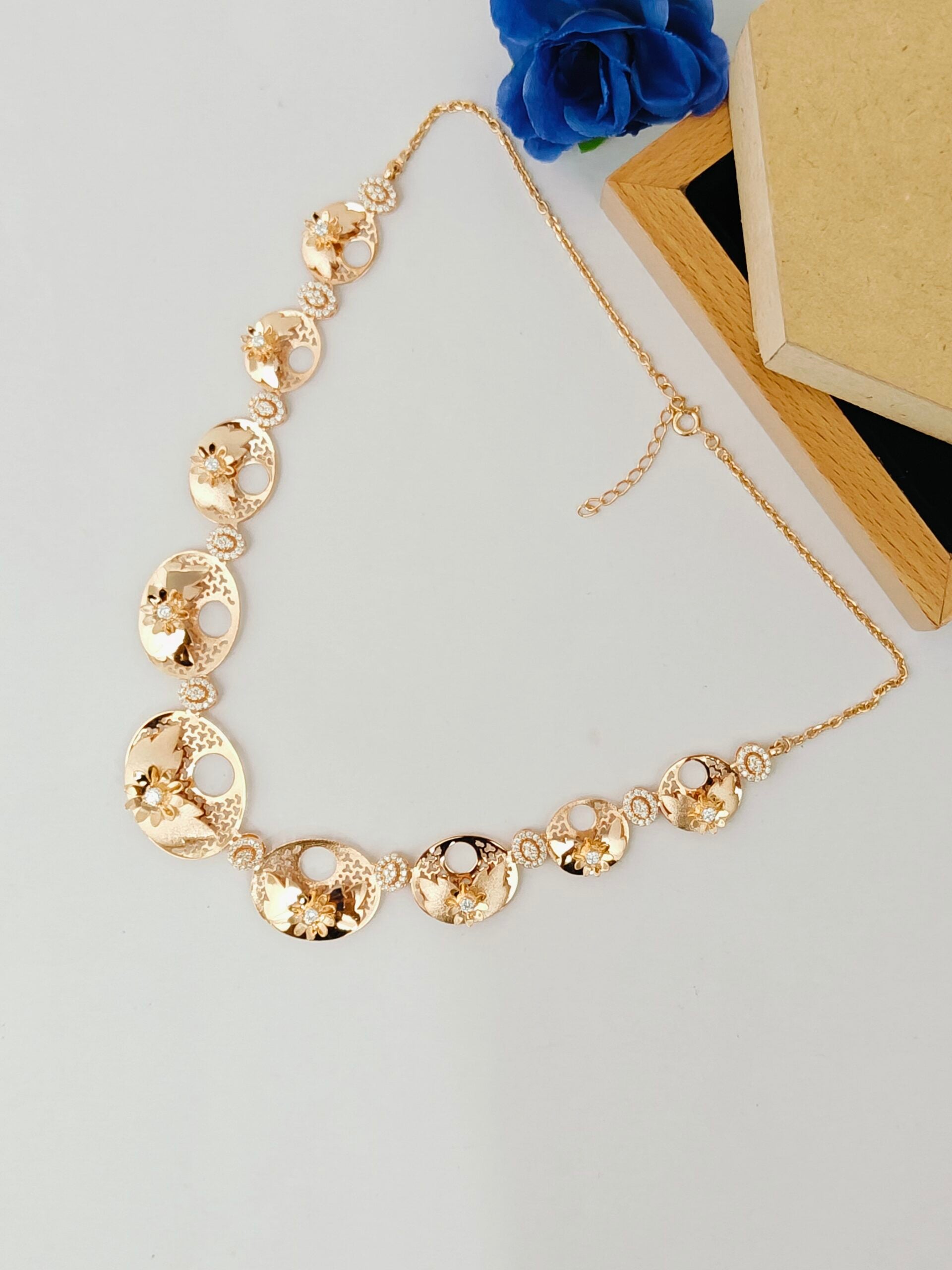 Gold necklace on a light gray surface with blue flowers and a wooden box in the background