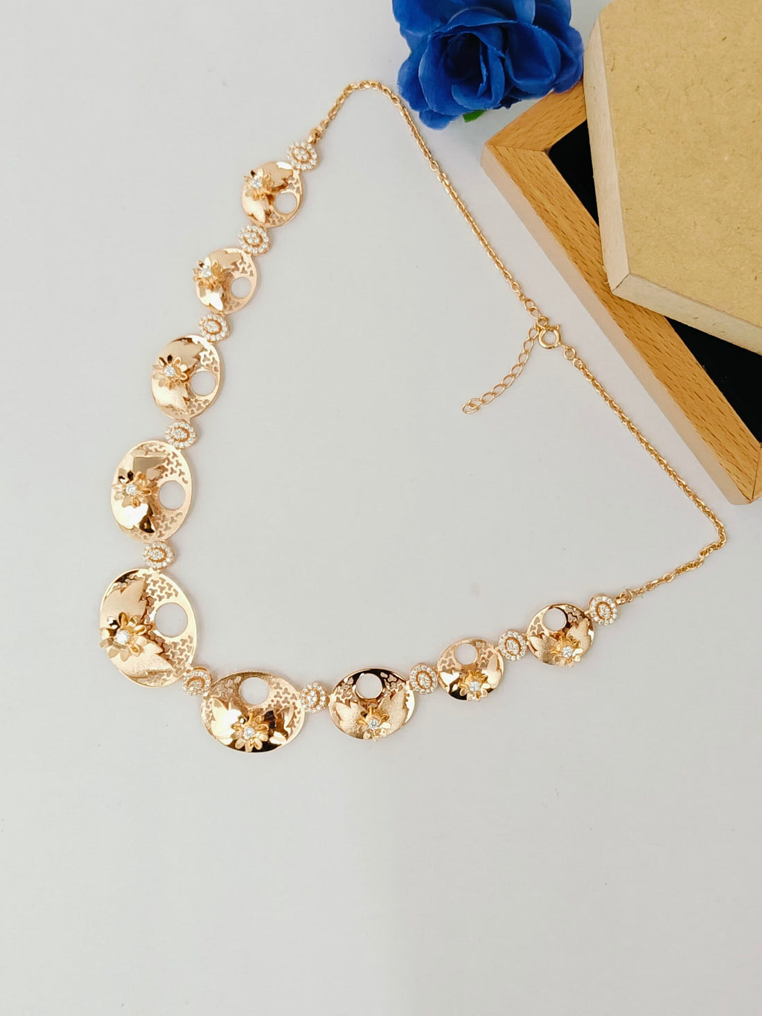 Gold necklace on a light gray surface with blue flowers and a wooden box in the background