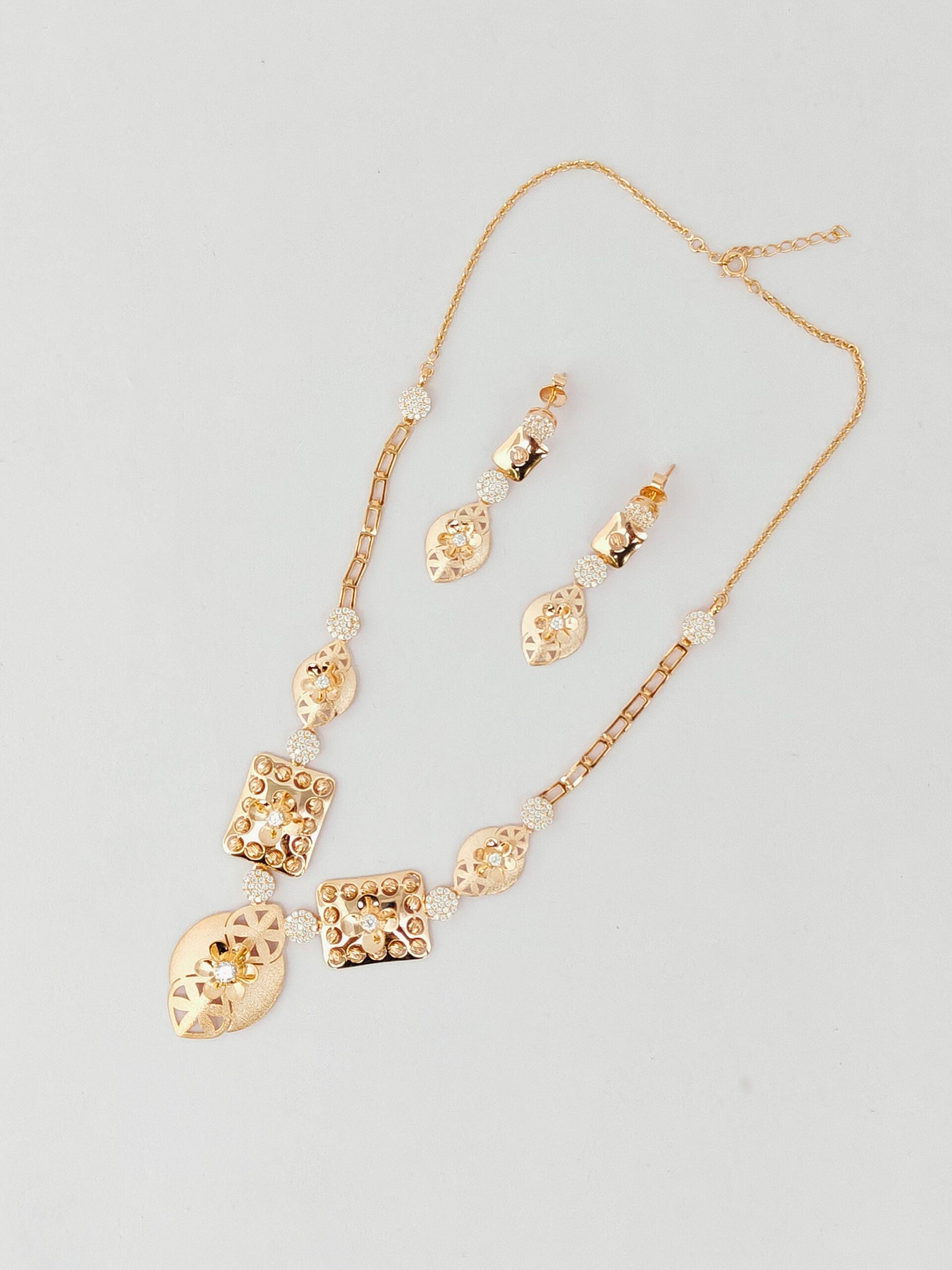 Gold necklace and earrings set on a light gray background