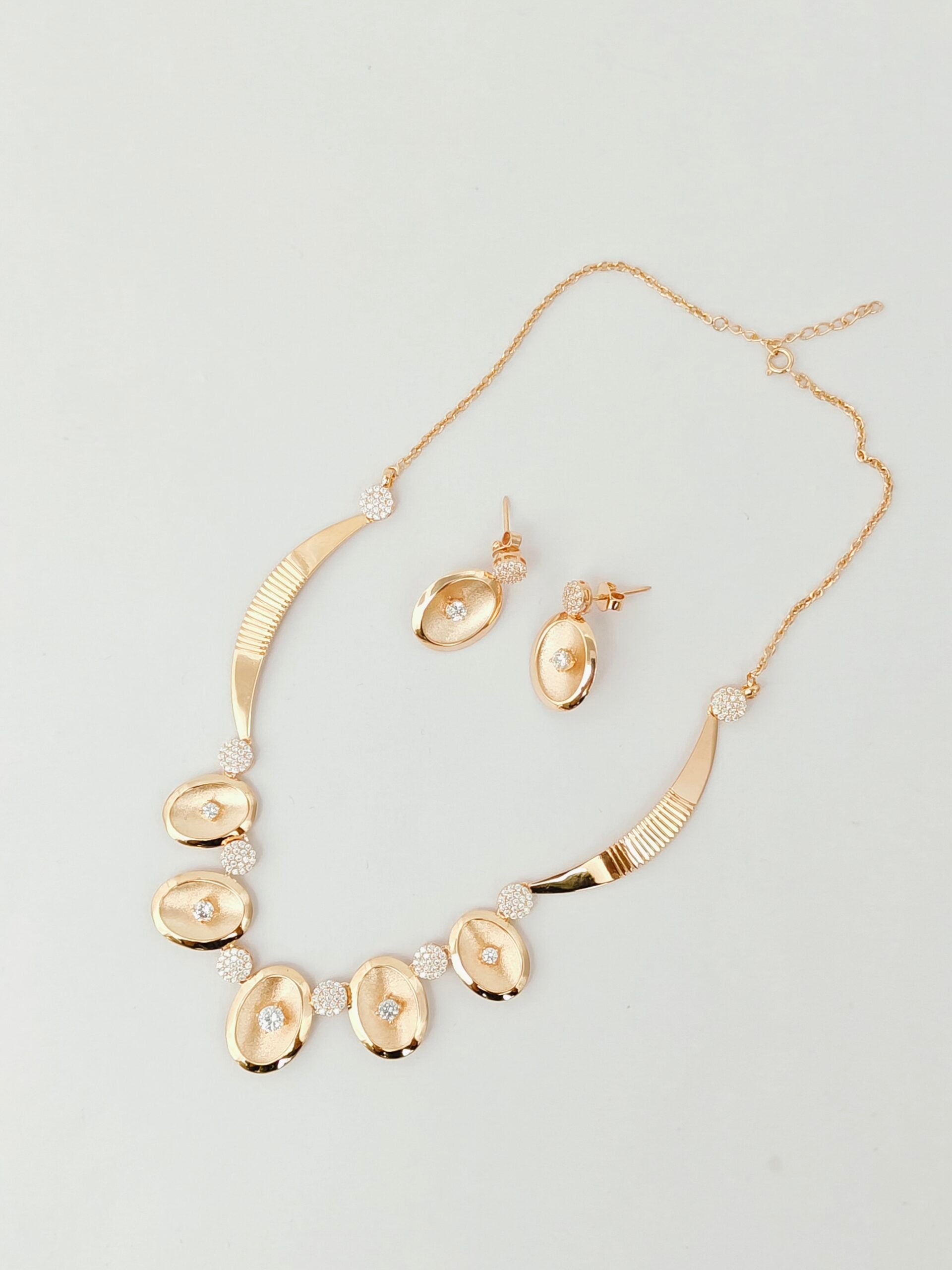 Gold necklace and earrings set on a light gray background