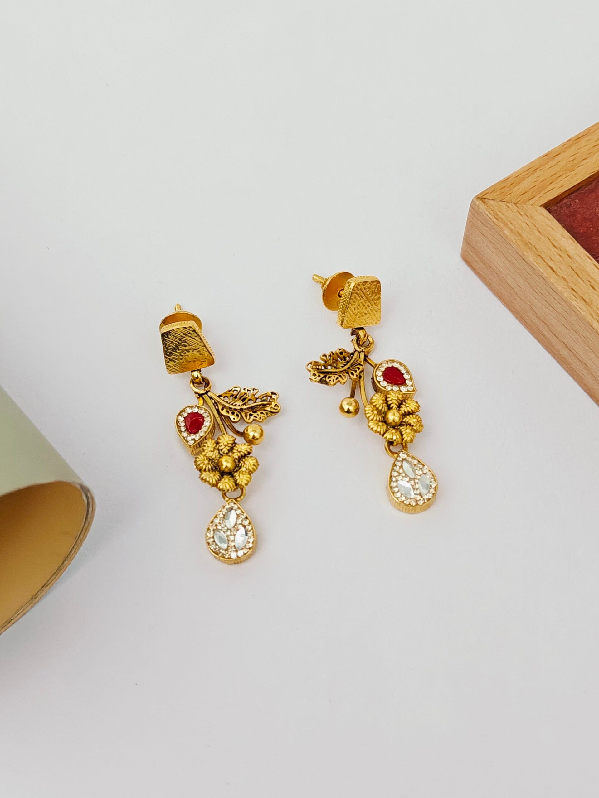 Gold earrings with red gemstones on a light gray background