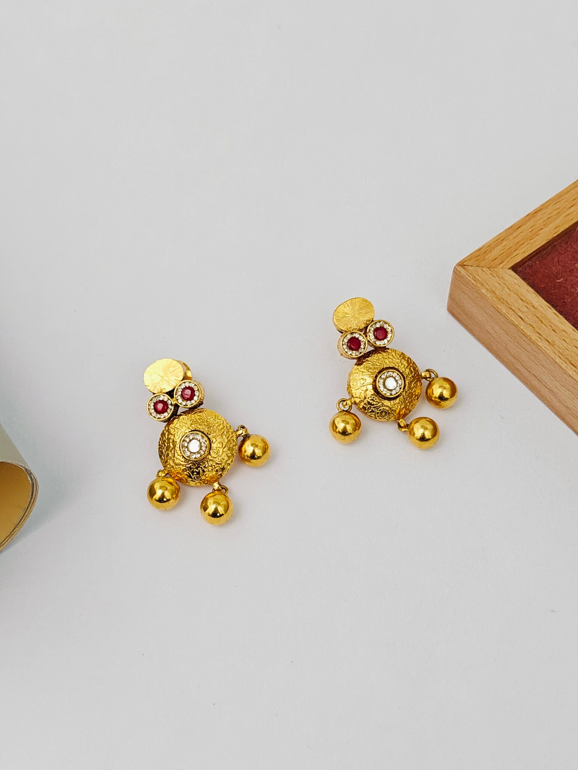Gold earrings with red gemstones on a light gray background