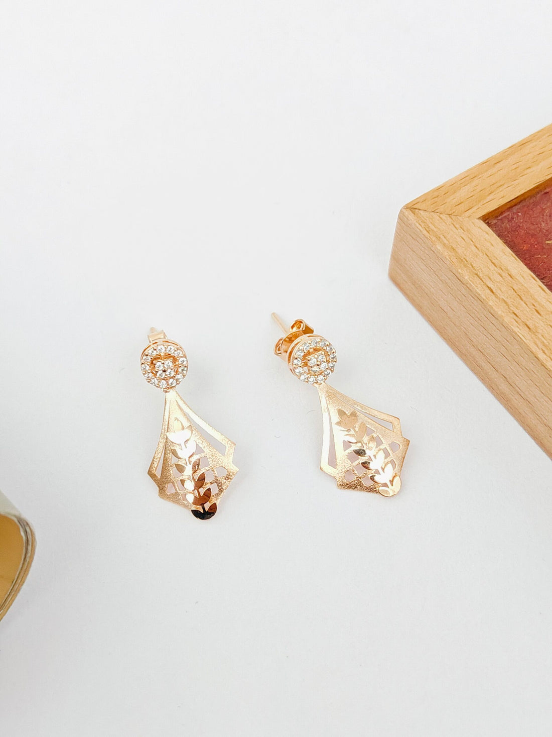 Gold earrings on a white surface with a wooden frame in the background